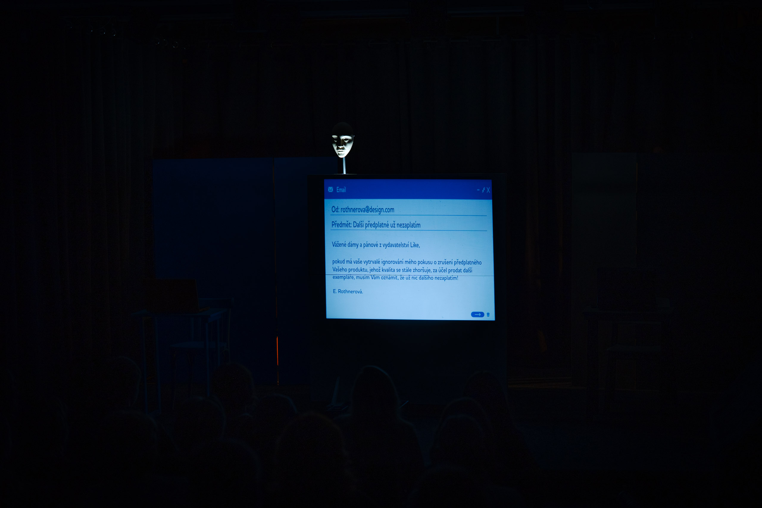 A mask is illuminated on a stand in front of a screen displaying