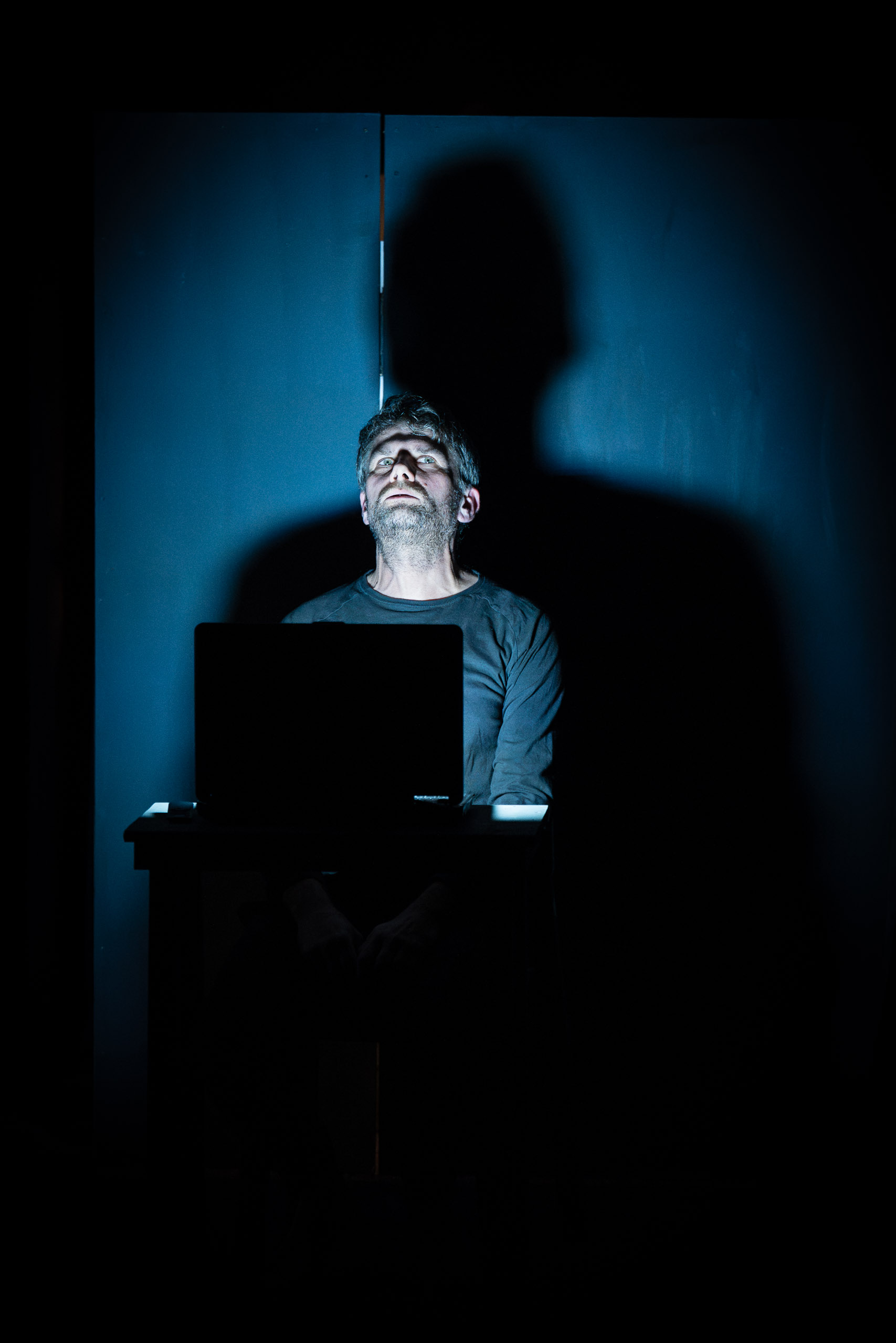 A man sits in front of a laptop, his face illuminated by a blue