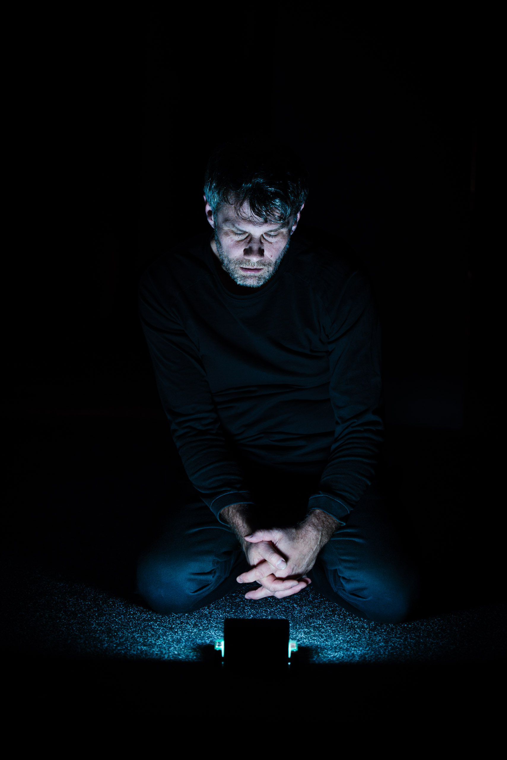 A man kneels in the dark, illuminated by the blue light of a pho