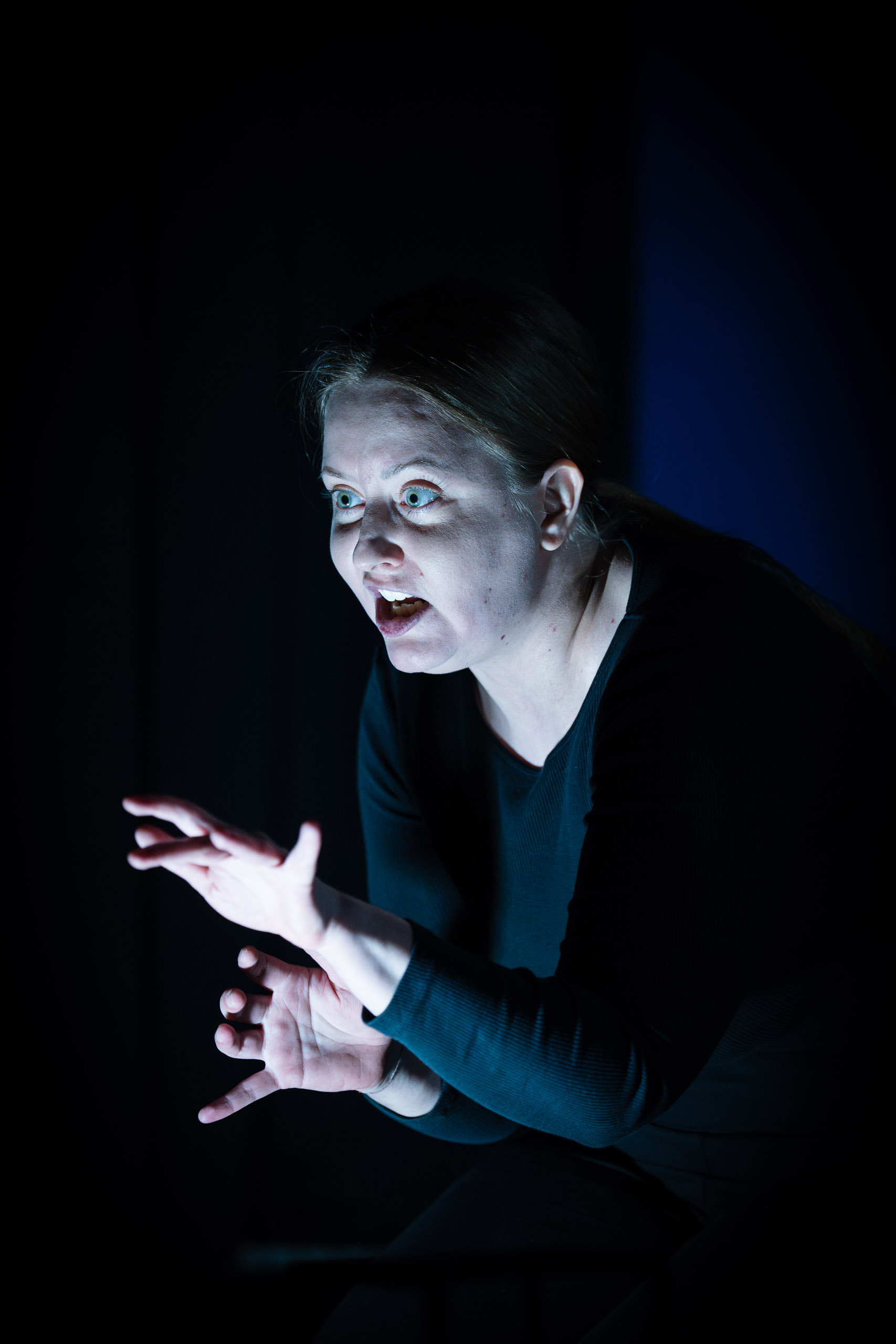 A woman with wide eyes and an open mouth gestures with her hands