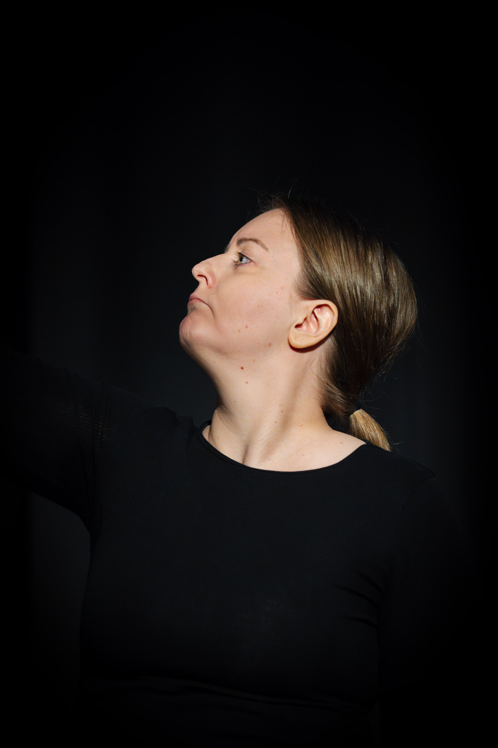 A woman in a black shirt looks up against a black background.