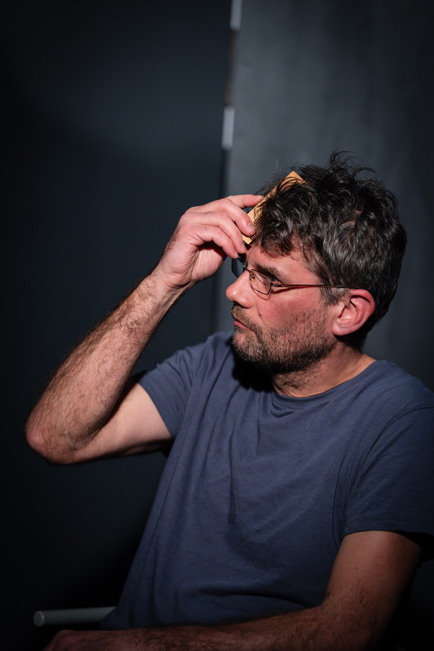 Man with glasses combing his hair with a wooden comb.