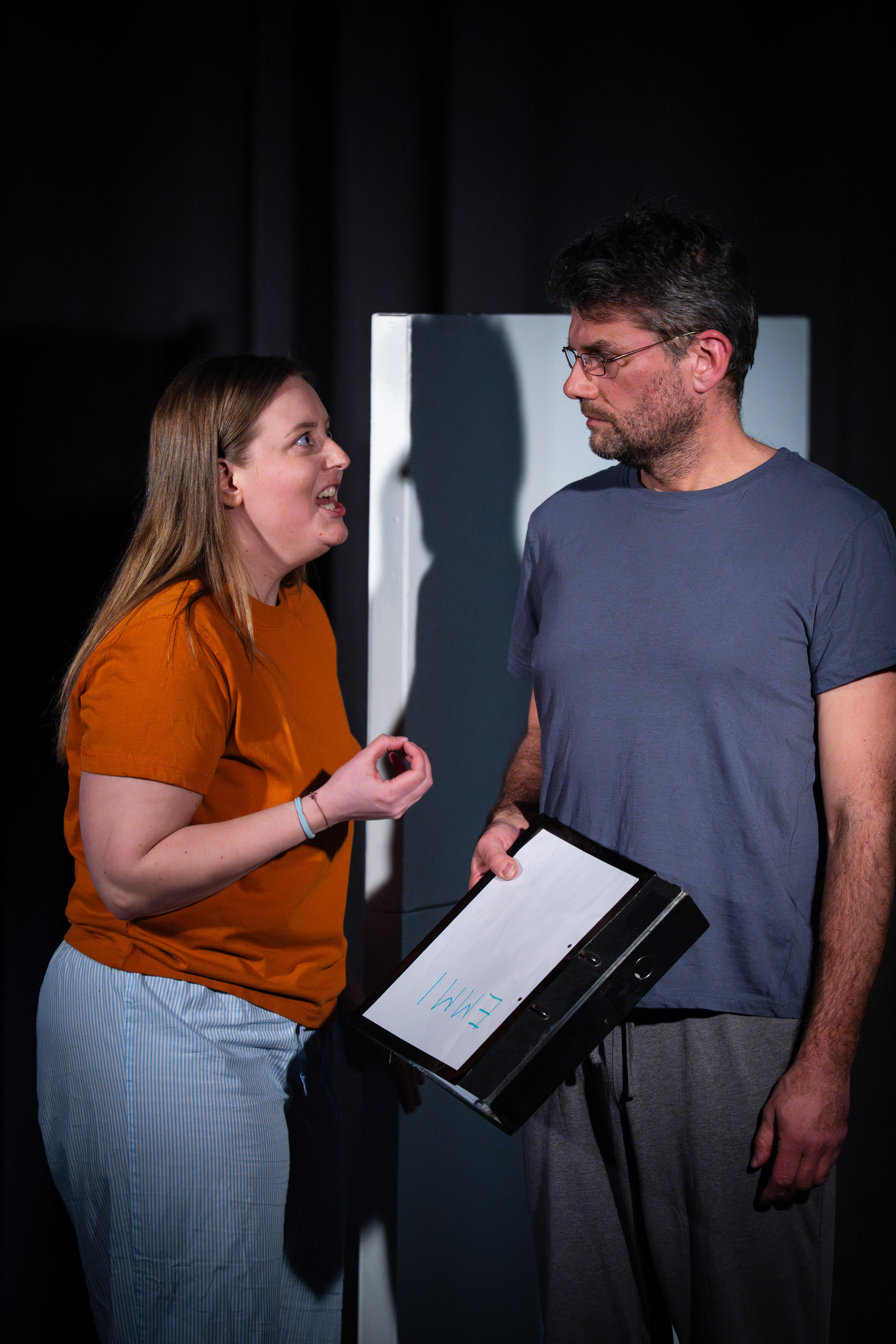 A woman argues with a man holding a binder with writing on it.