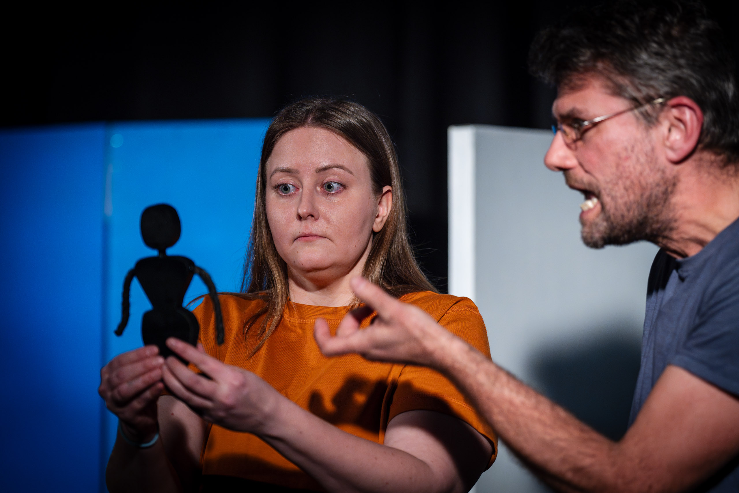 A woman holds a puppet while a man gestures emphatically during