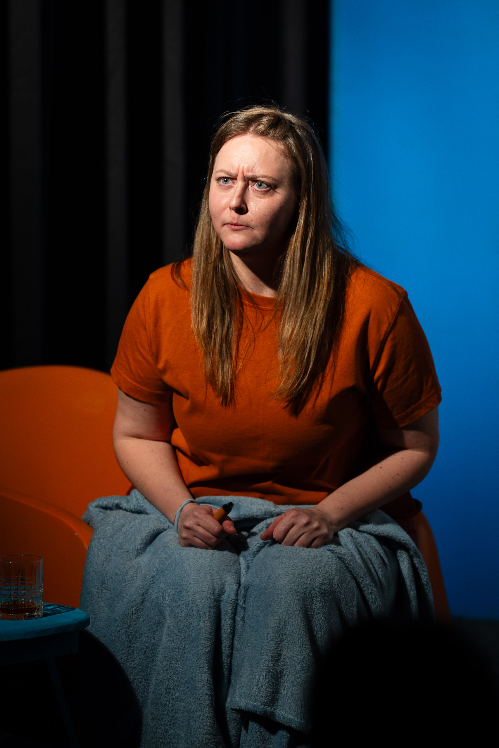 A woman sits wrapped in a blanket, looking concerned.