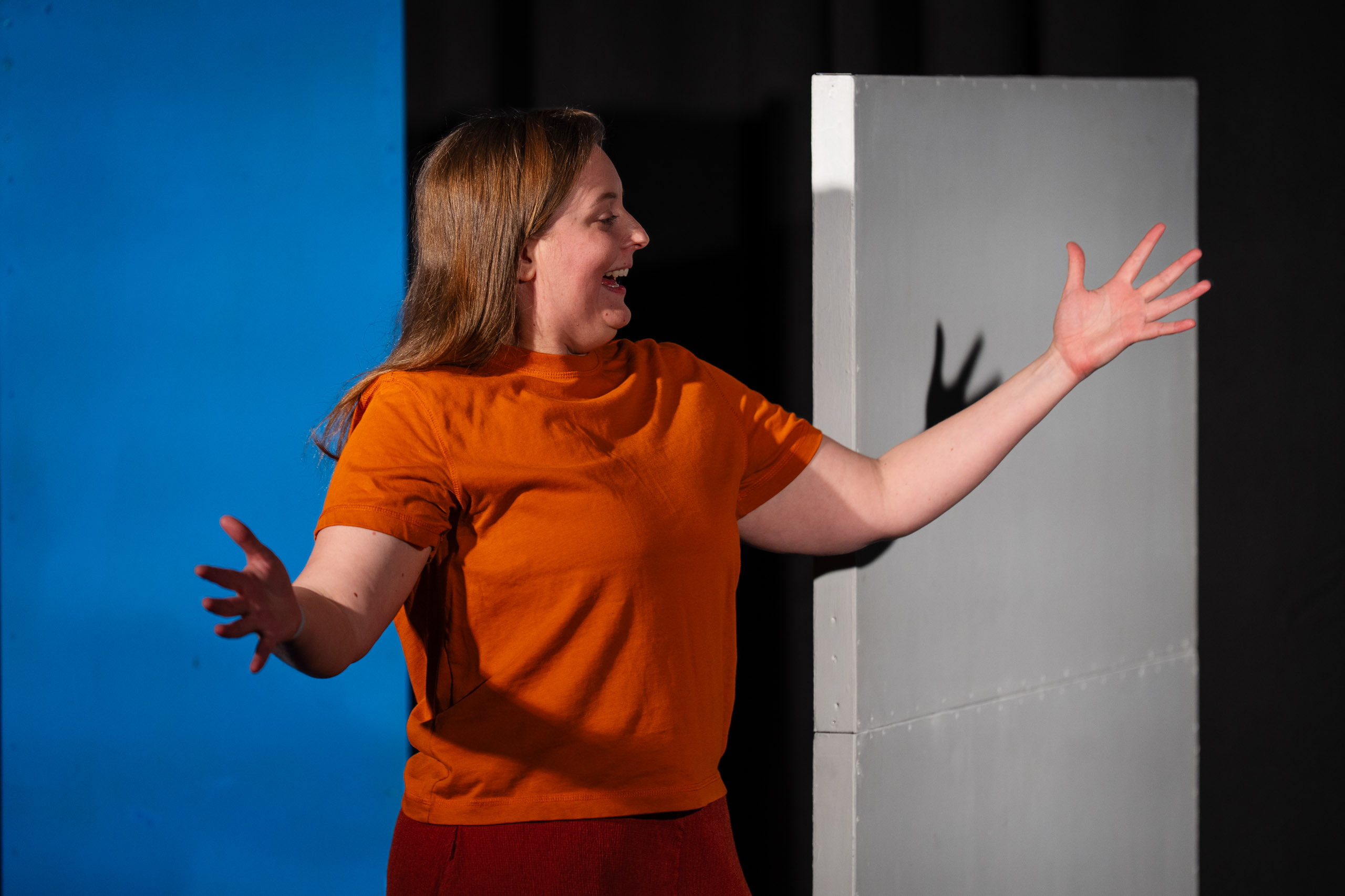 A woman in an orange shirt gestures with her hands while on stag