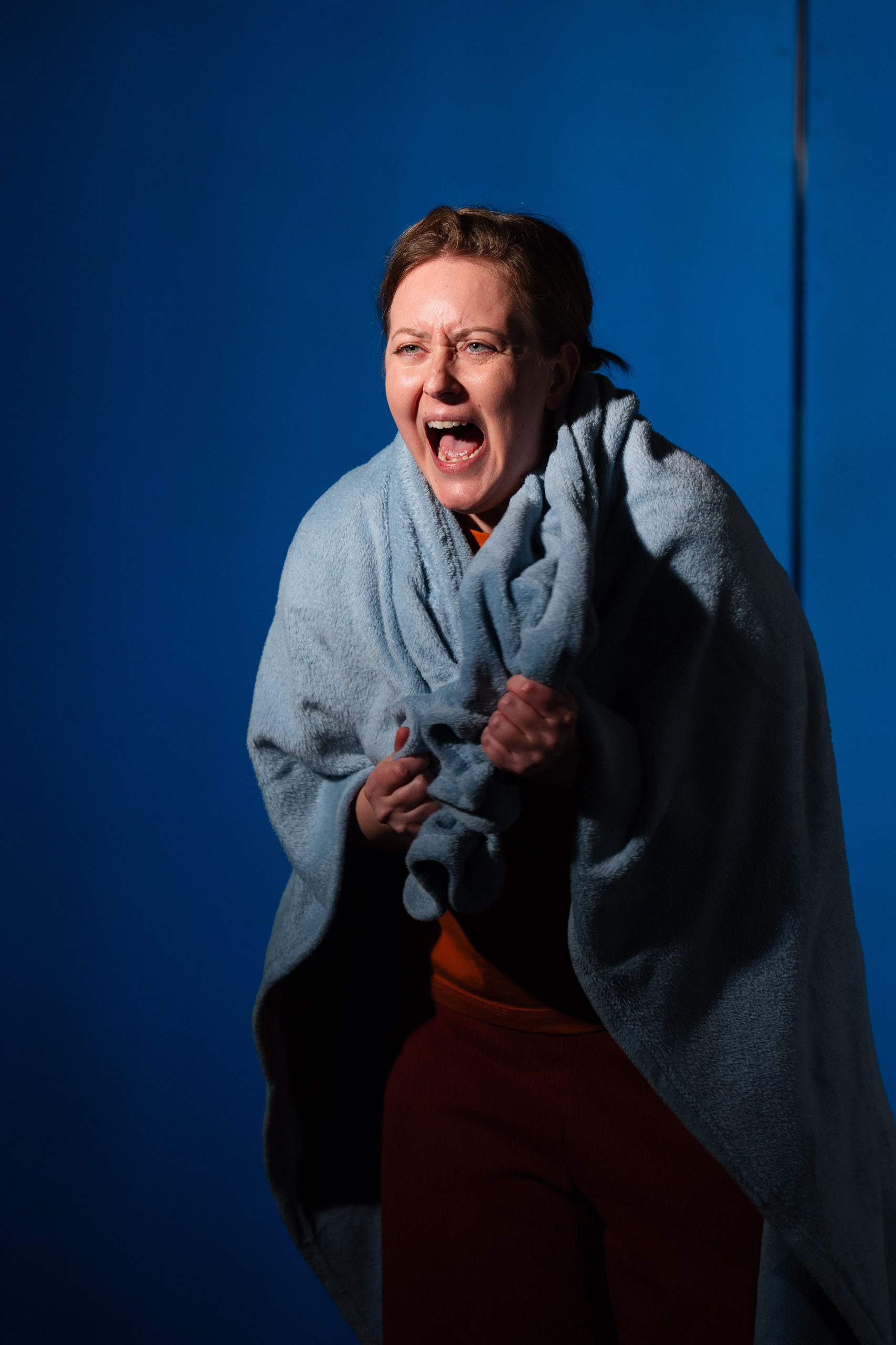 A woman wrapped in a blue blanket screams in distress against a