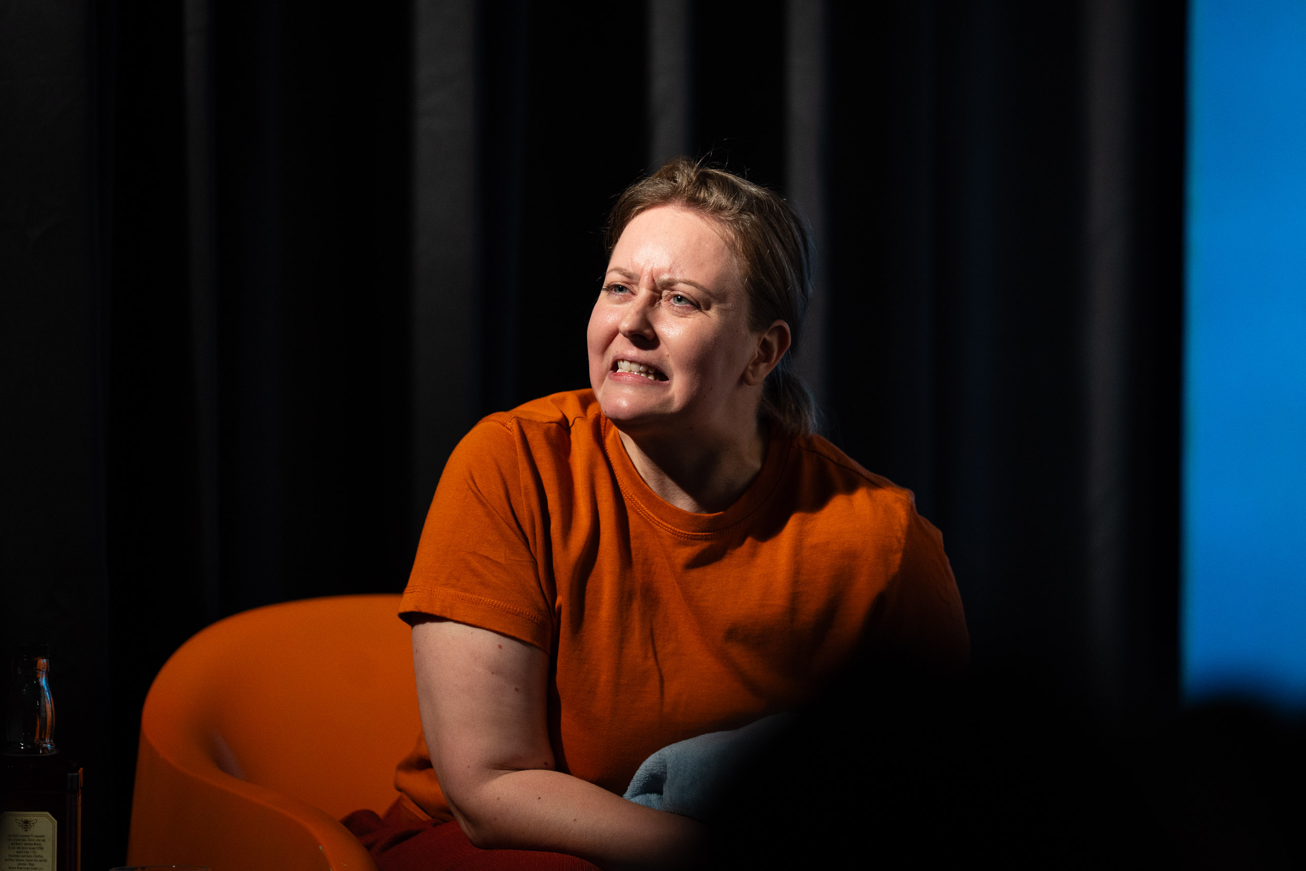 A woman in an orange t-shirt sits in an orange chair with a dark