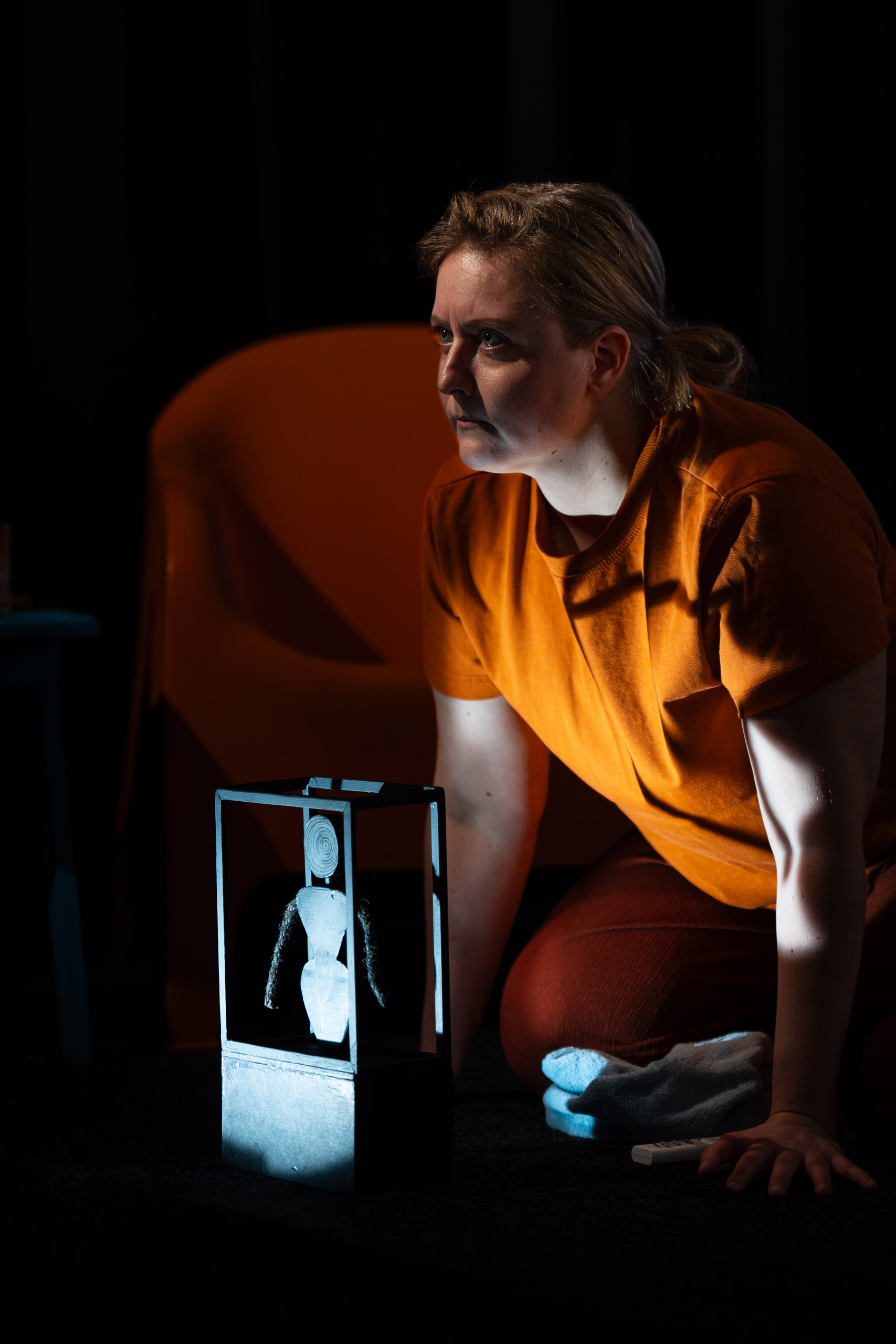 A woman kneels in front of a small illuminated figure in a box,