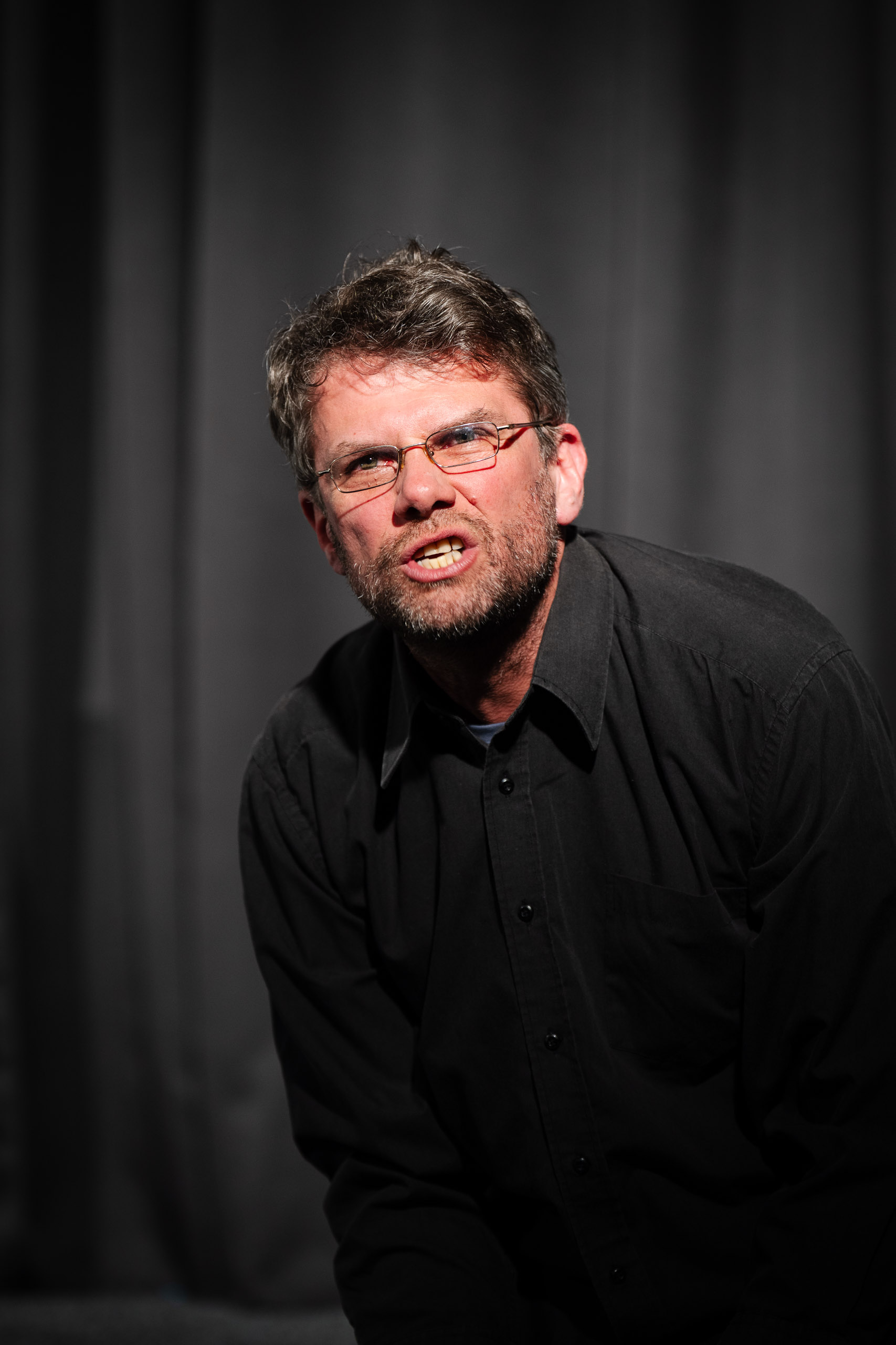 A man with glasses and a beard speaks with his mouth open.