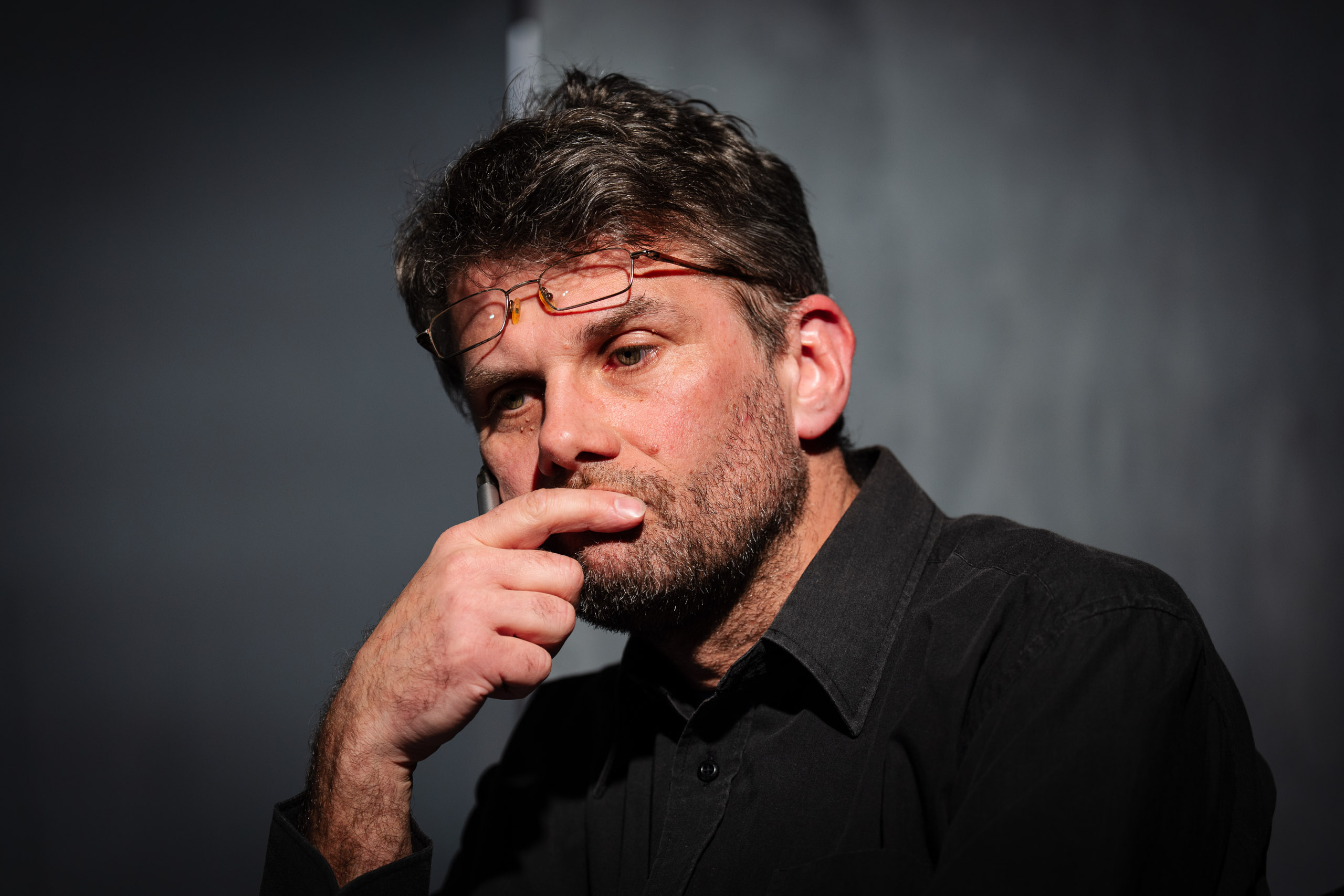 A man with glasses and a beard, with his finger to his lips, loo