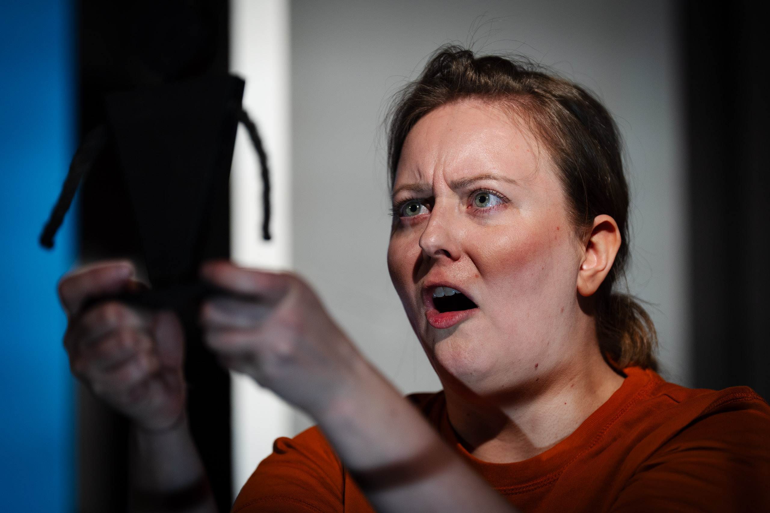 A woman with an orange shirt and green eyes looks shocked while