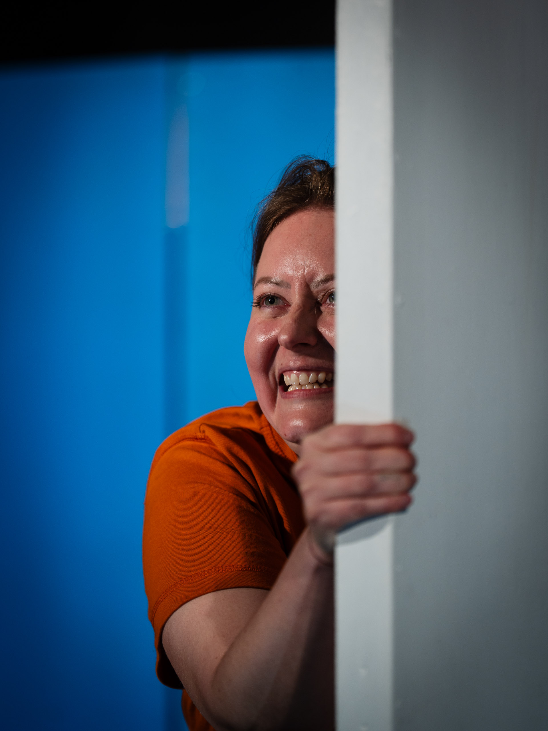 A woman peeks around a corner with a strained expression.
