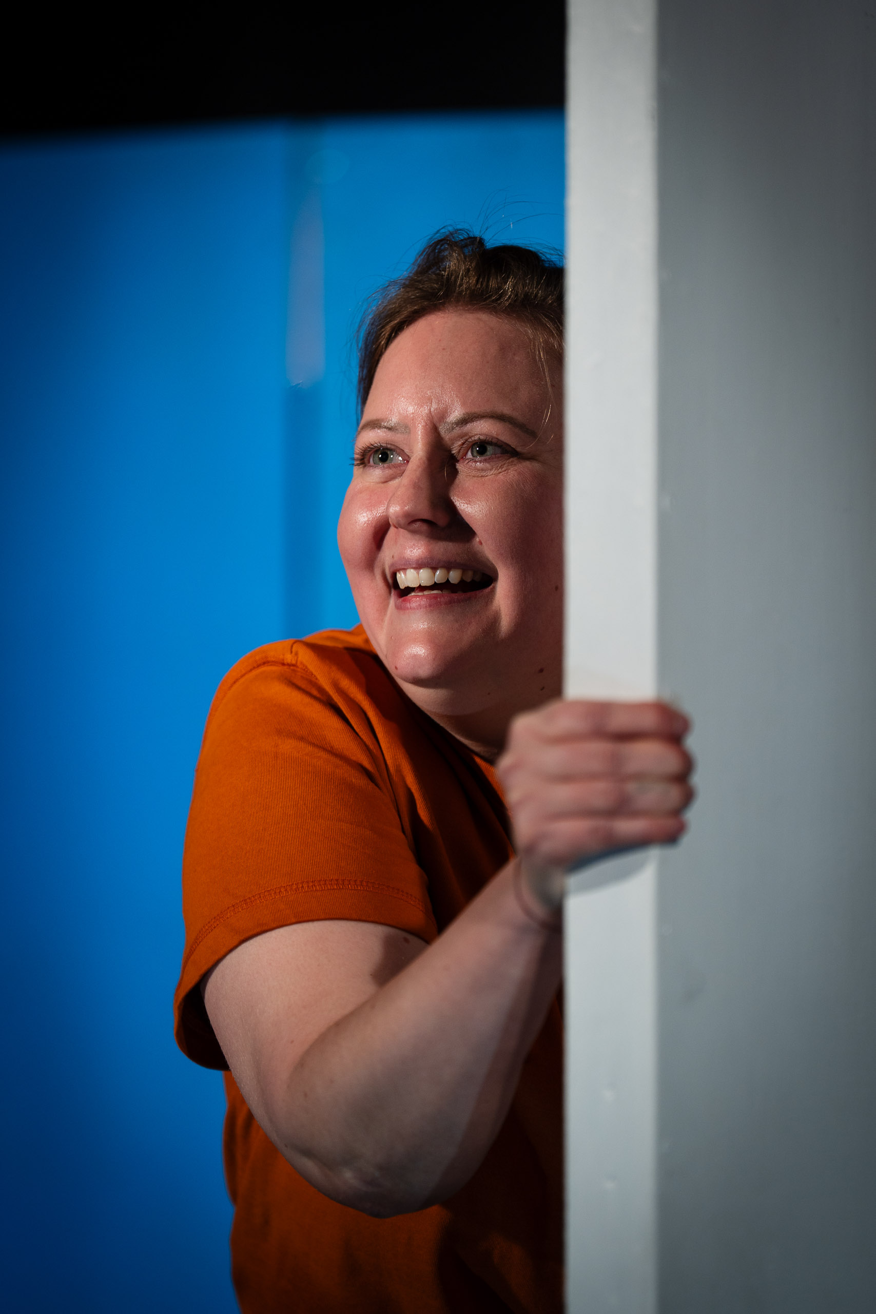 A woman peeks around a corner, smiling broadly.