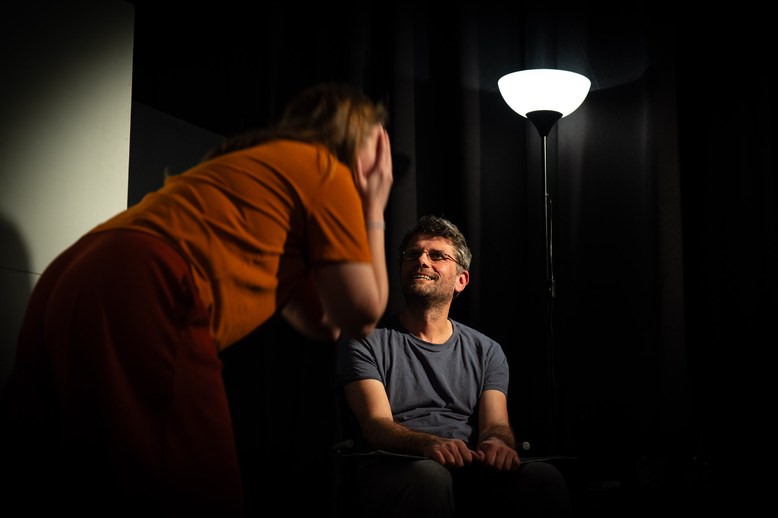 A man smiles as a woman covers her face in a dimly lit room with