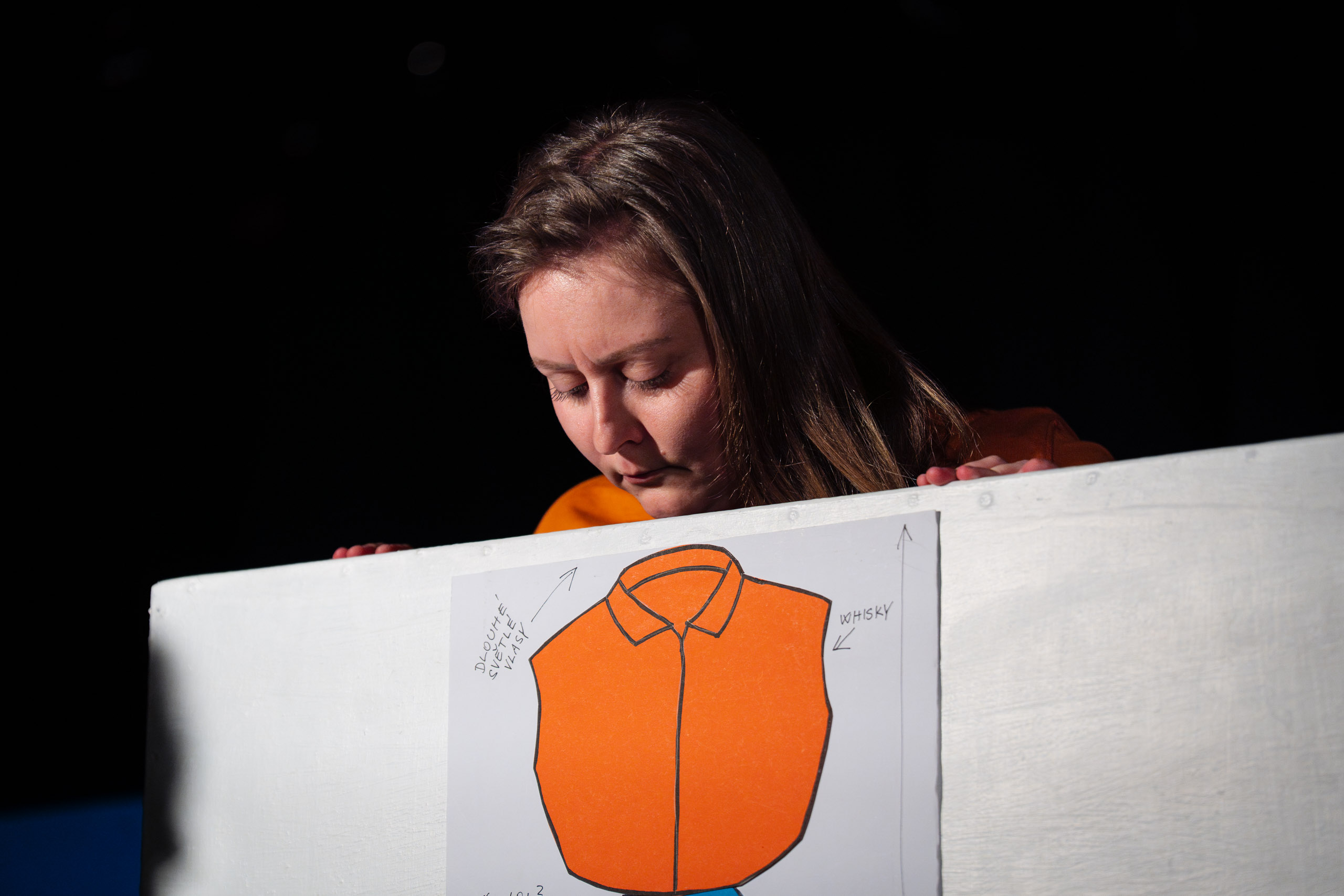 A woman looks down at a drawing of an orange shirt with labels.