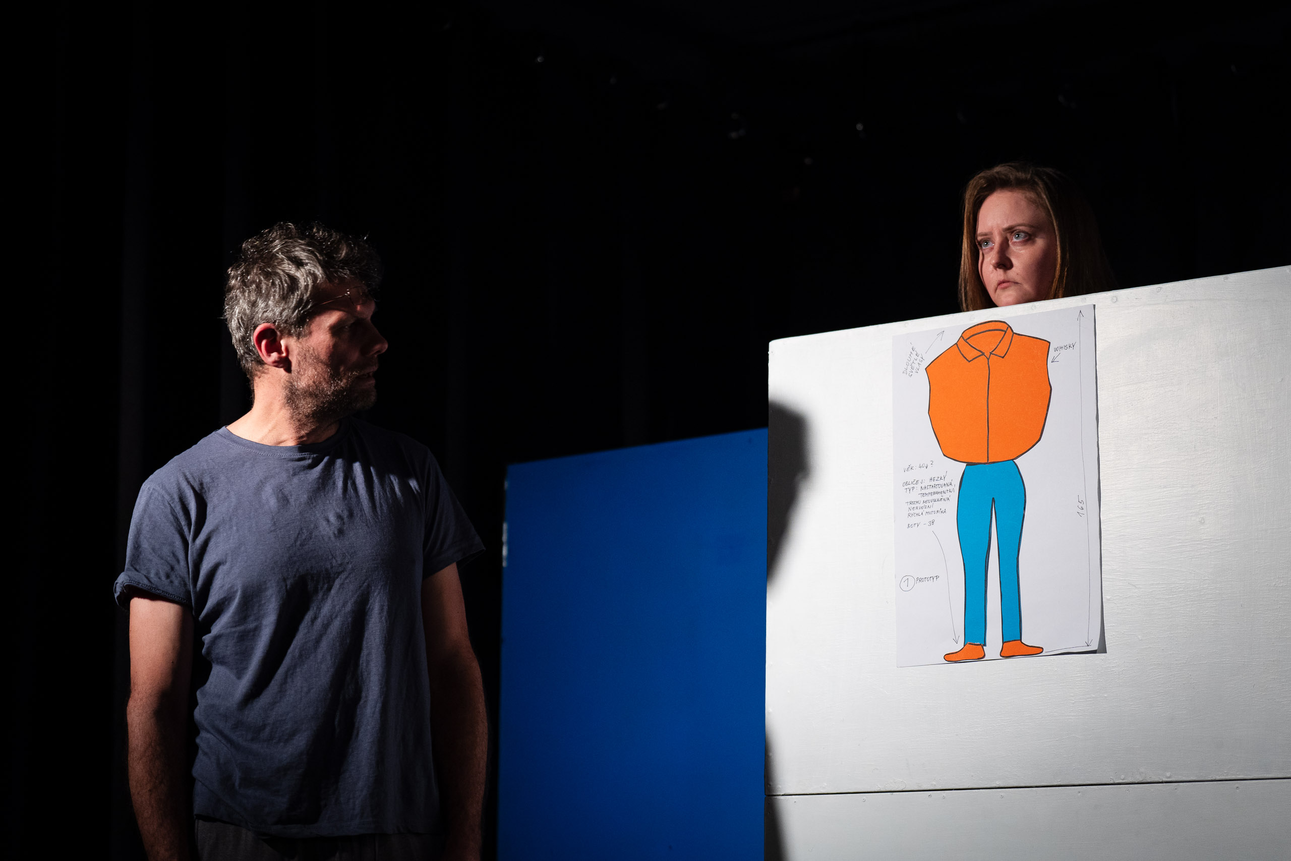 A man and a woman look at a drawing of a person's outfit on a wh