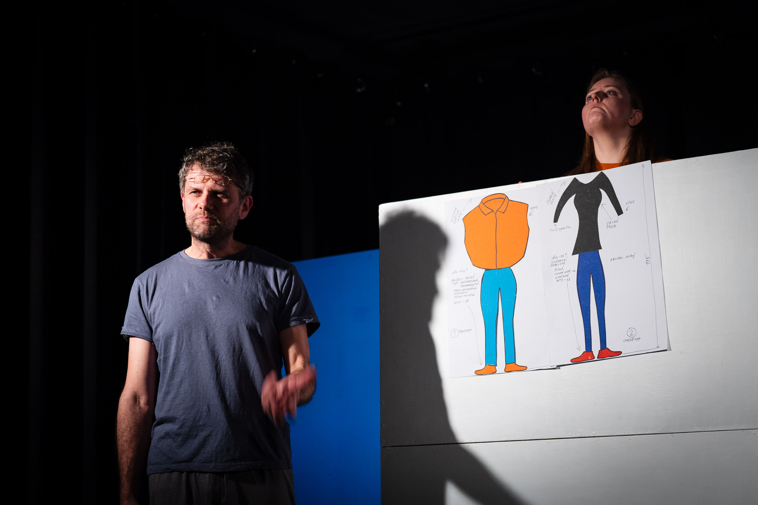 A man and a woman are on stage, with a drawing of clothing desig