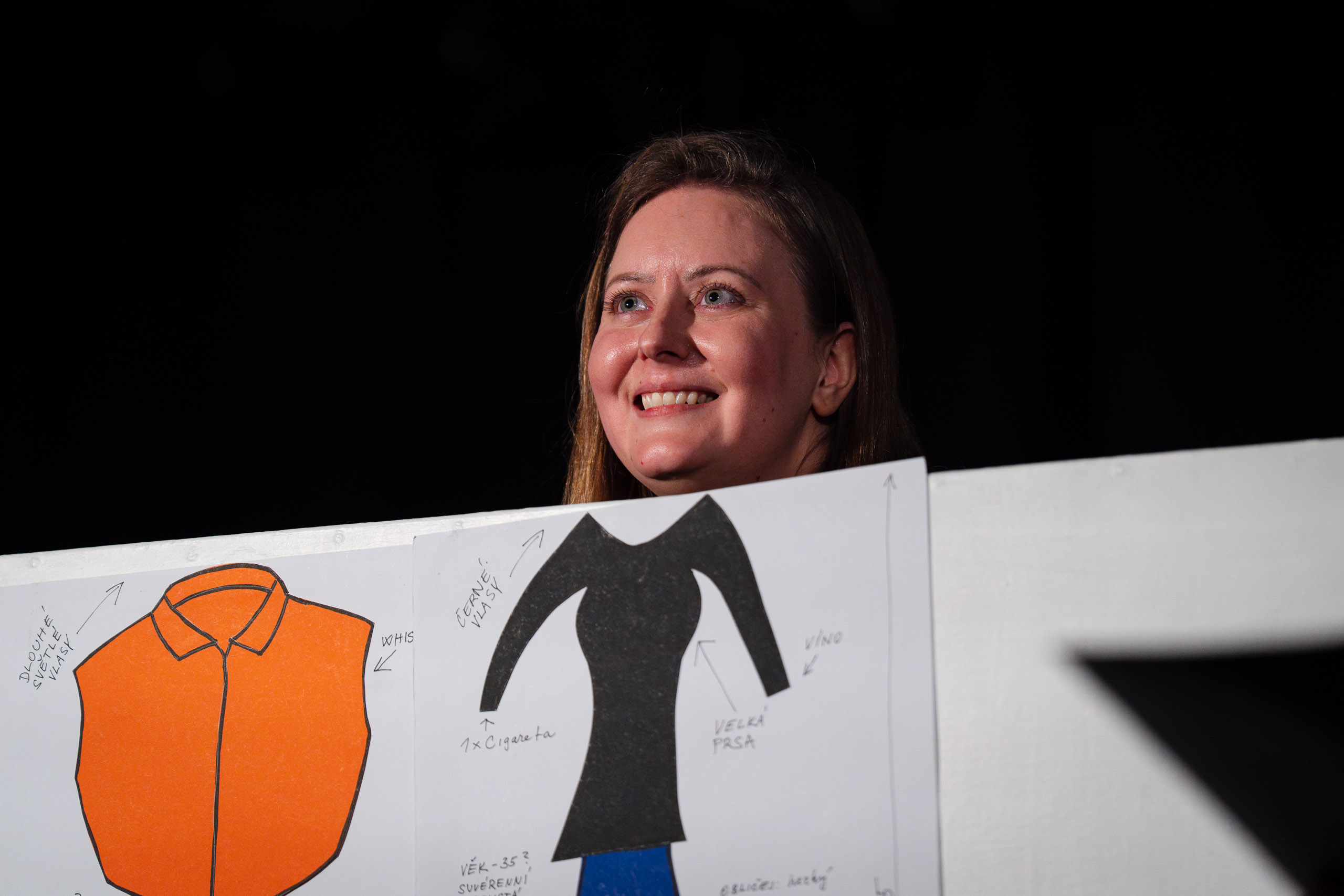 A woman smiles while holding up drawings of clothing designs.