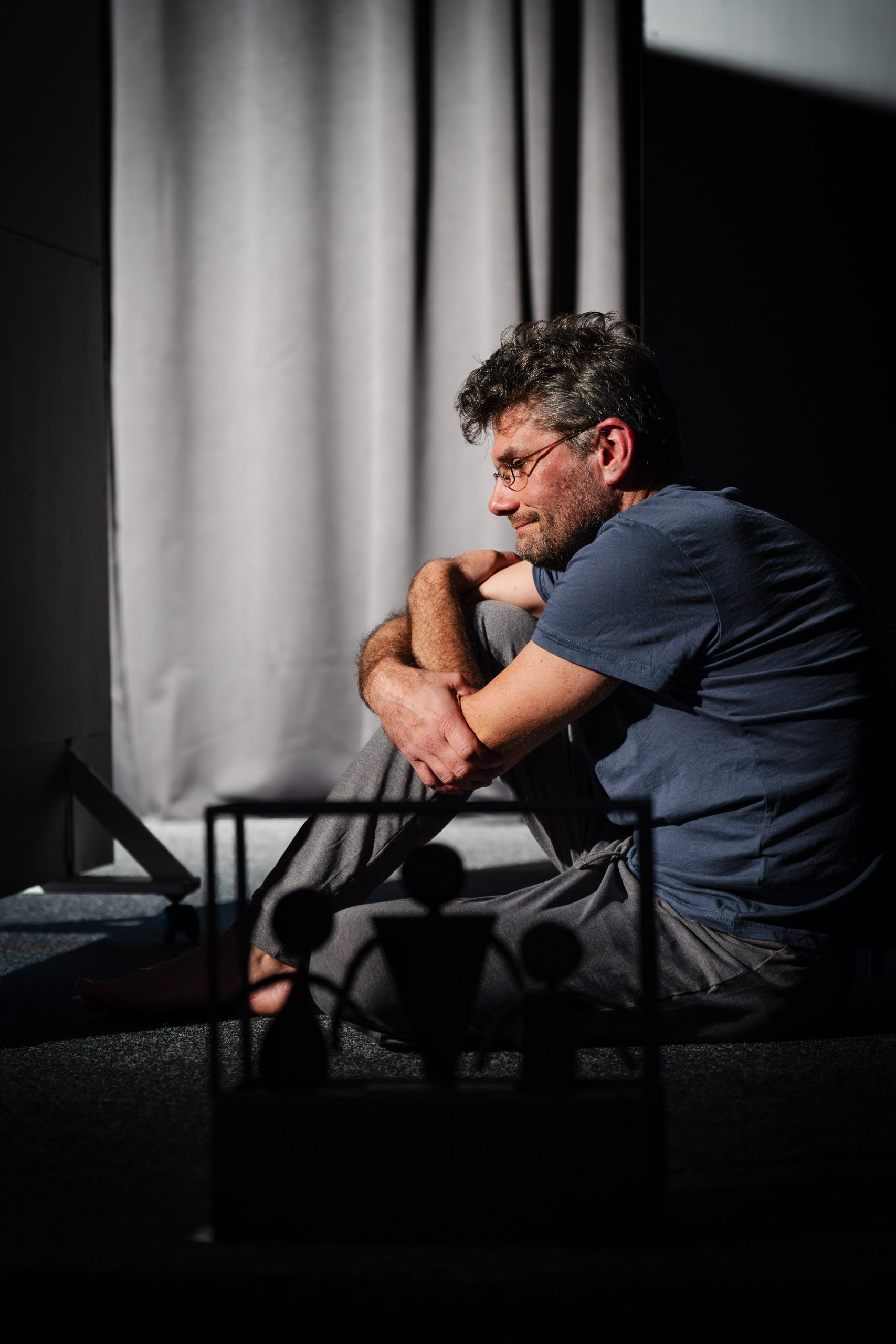 A man sits on the floor, looking down with his arms crossed.