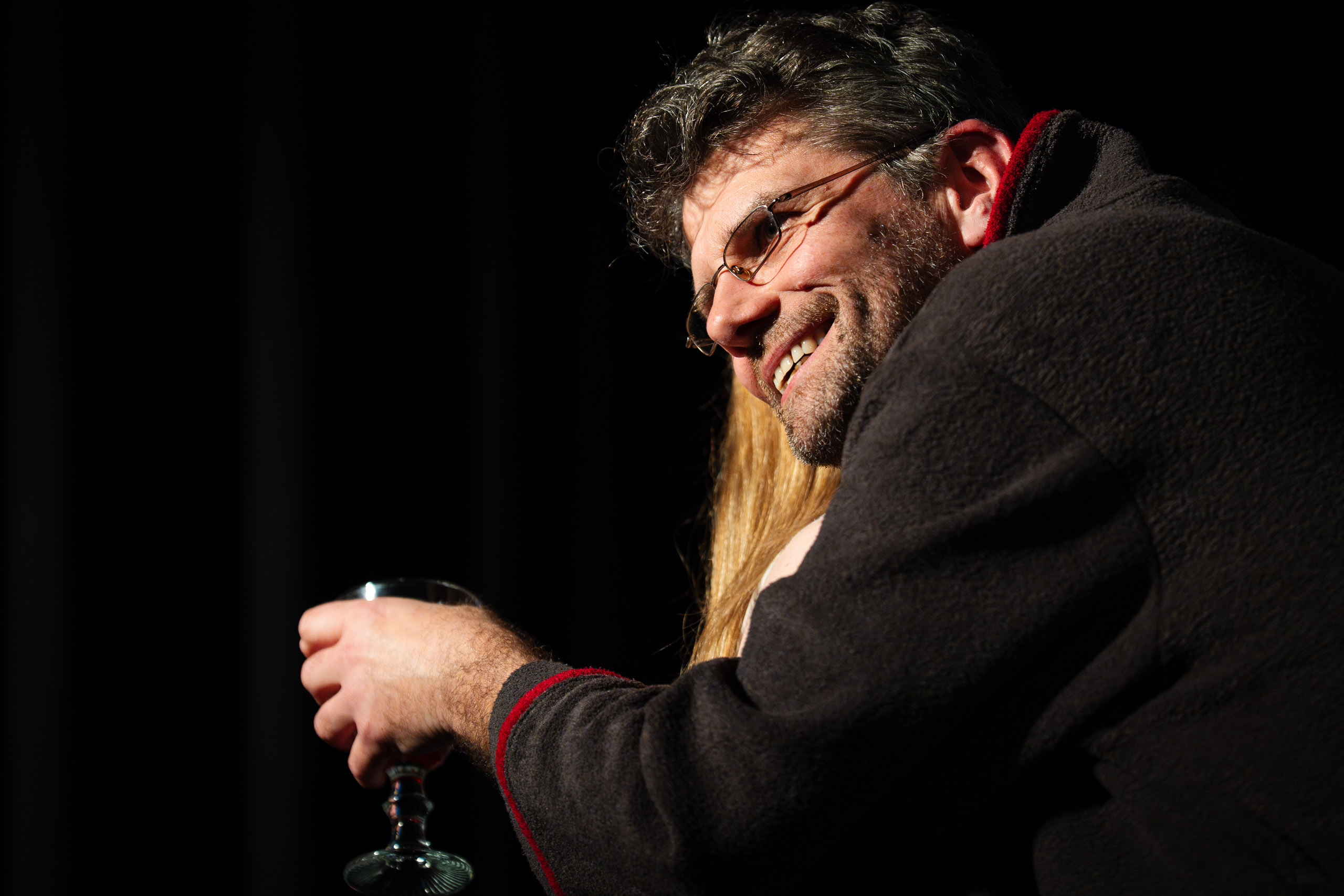 A man with glasses smiles and holds a glass of wine.