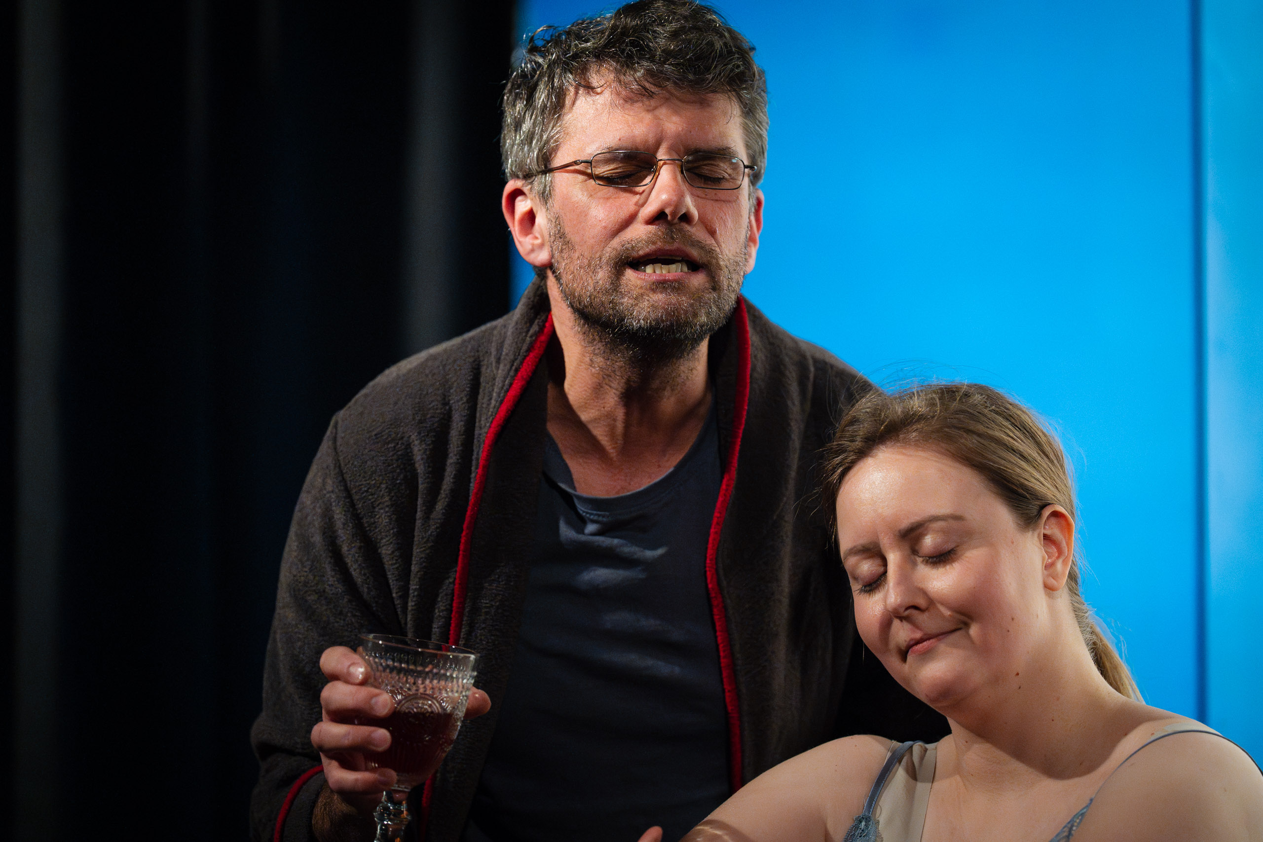 A man with glasses and a woman with her eyes closed, possibly in