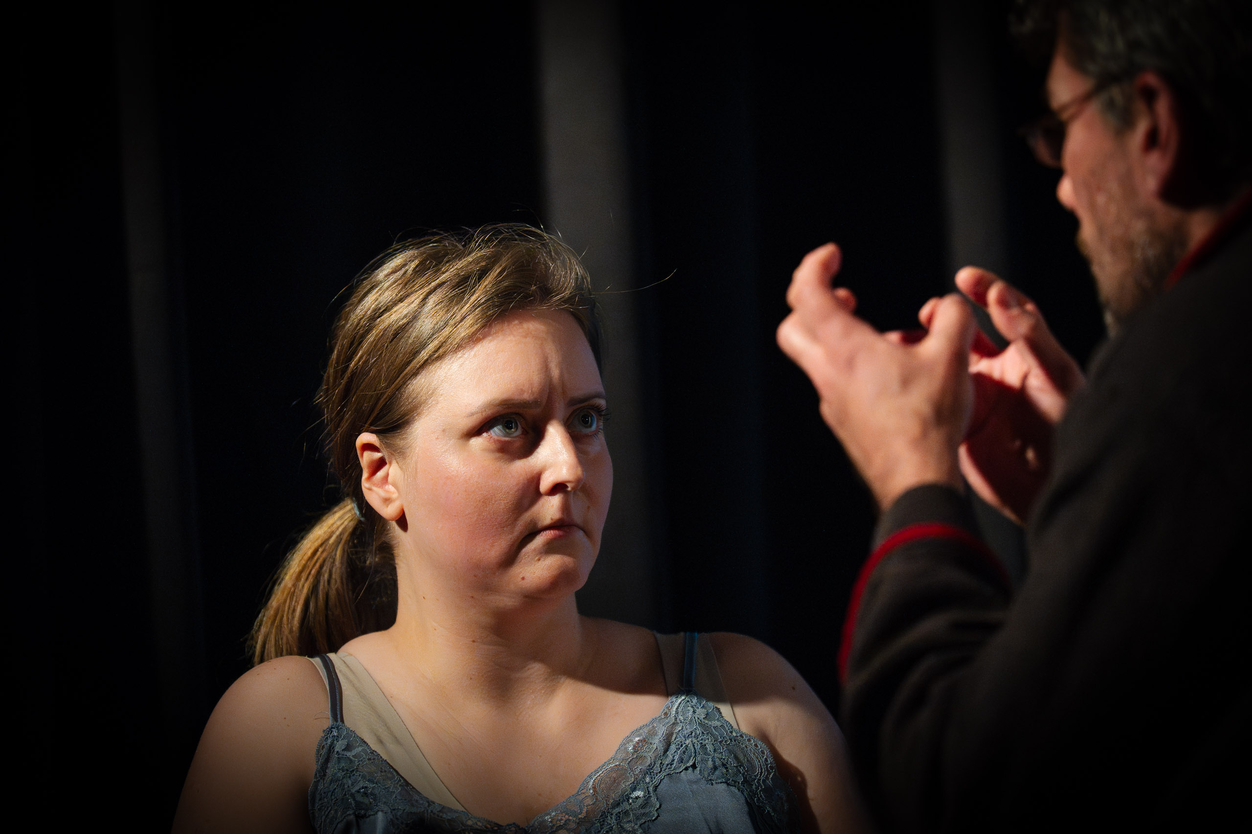 A woman looks intently at a man gesturing with his hands, sugges