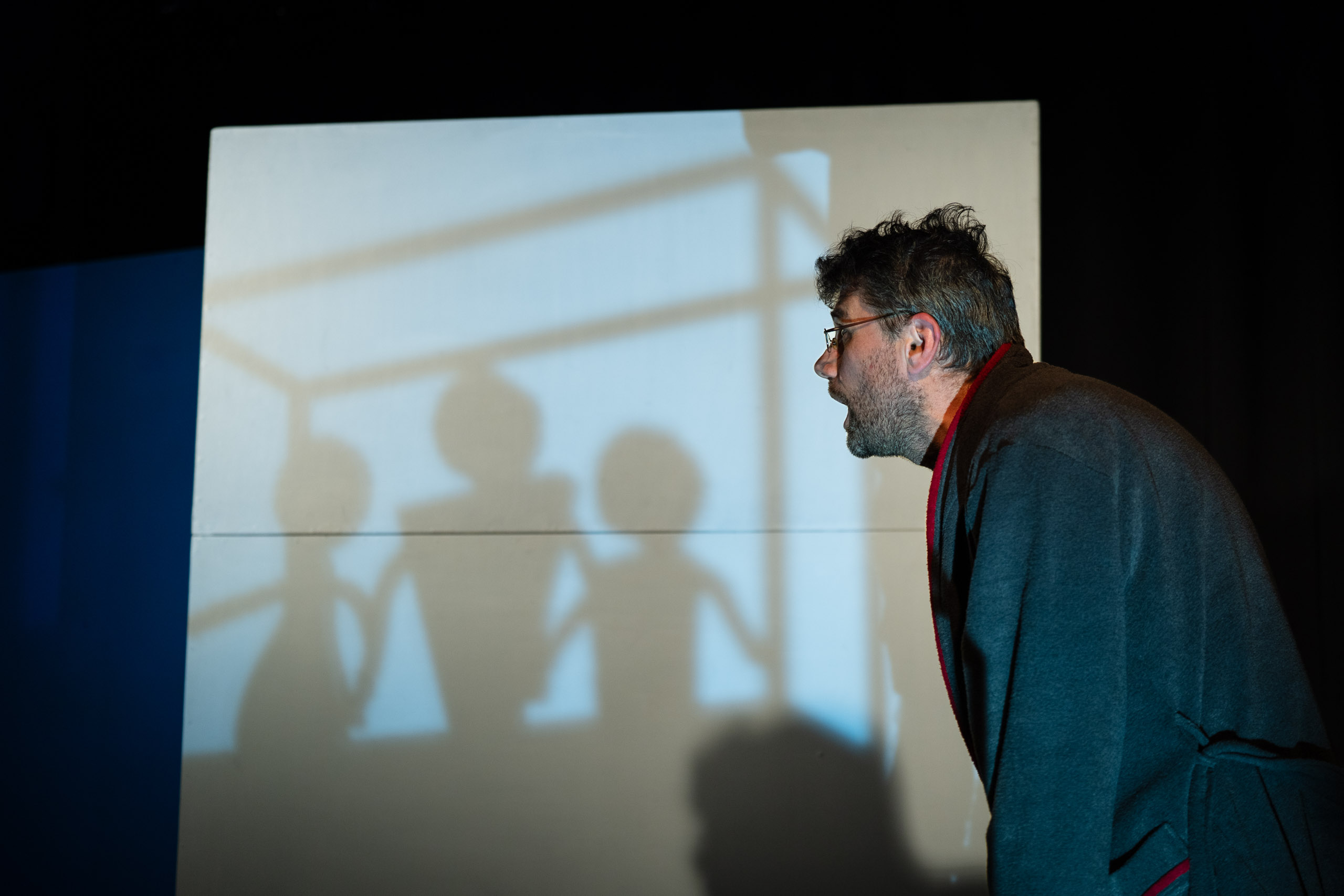 A man in a robe looks at shadows on a screen, possibly during a