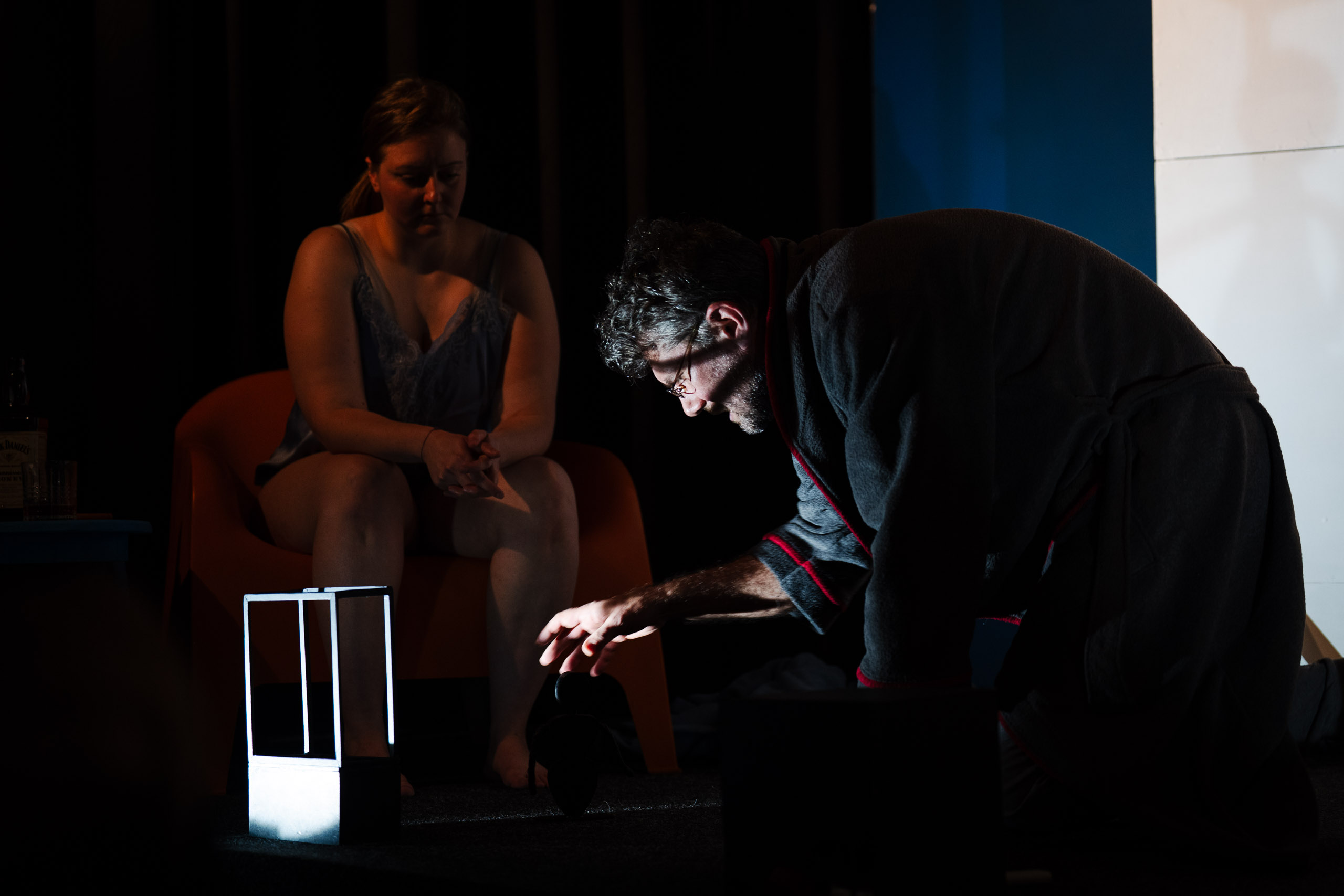 A man in a robe kneels before a woman sitting in a chair, reachi