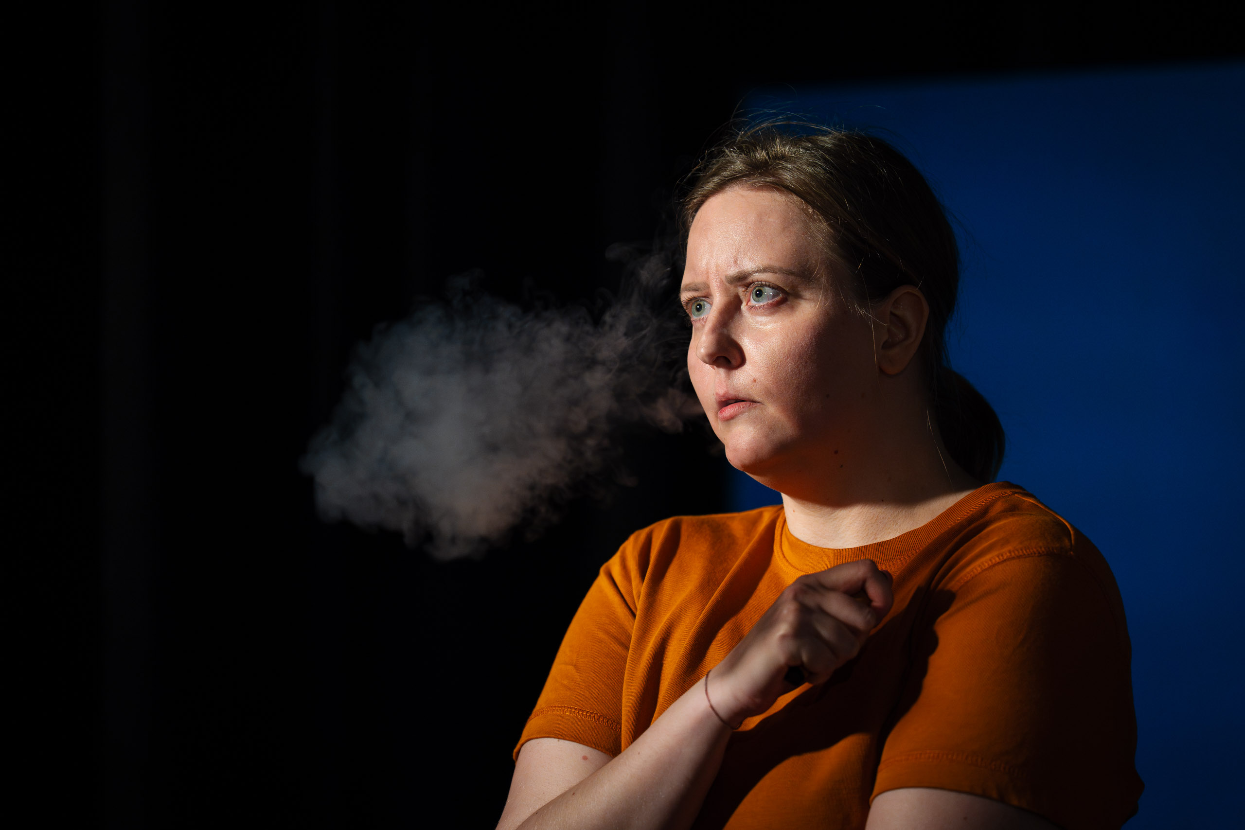 A woman exhales a cloud of smoke or vapor against a dark backgro
