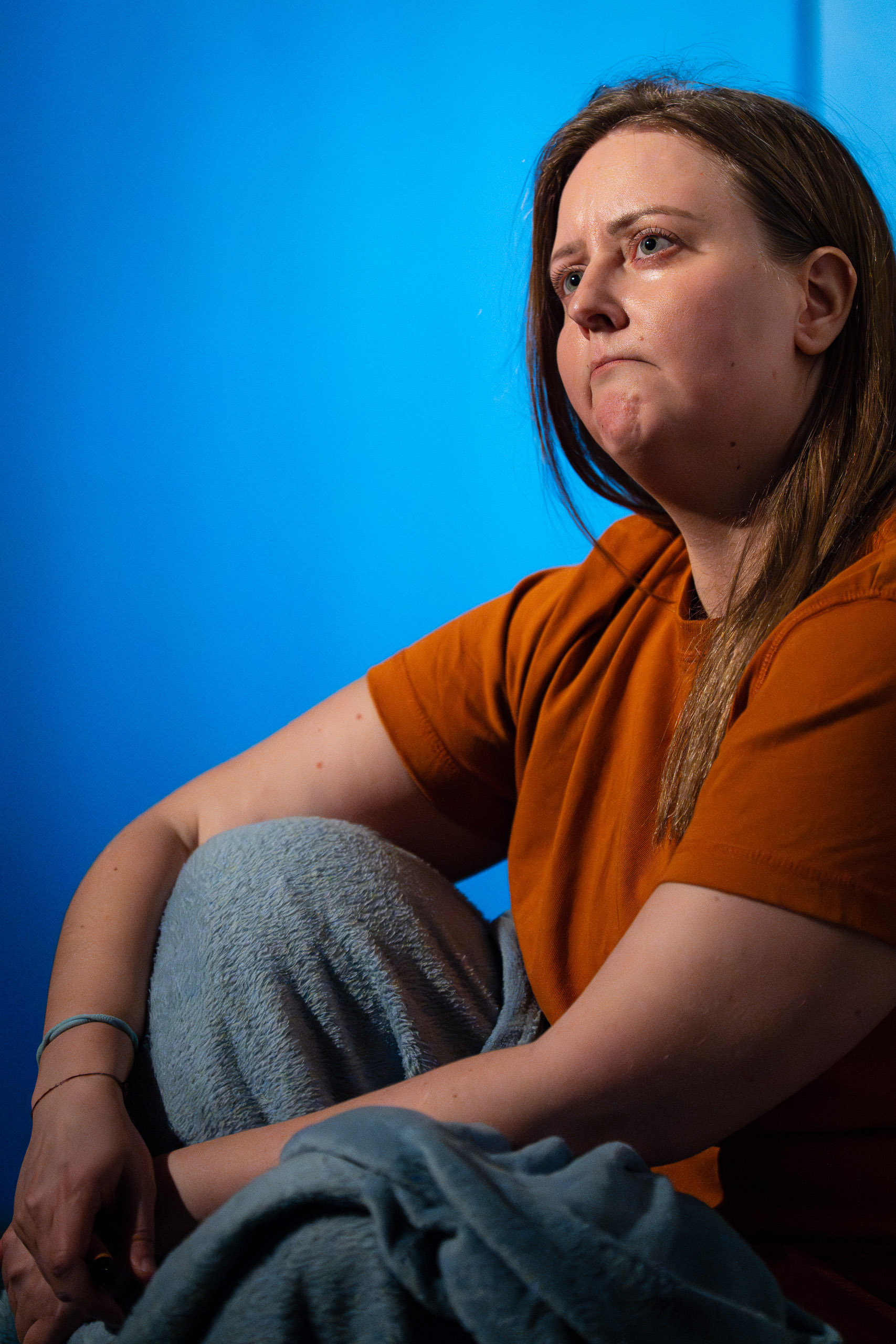 A woman sits with her knees pulled to her chest, looking away wi