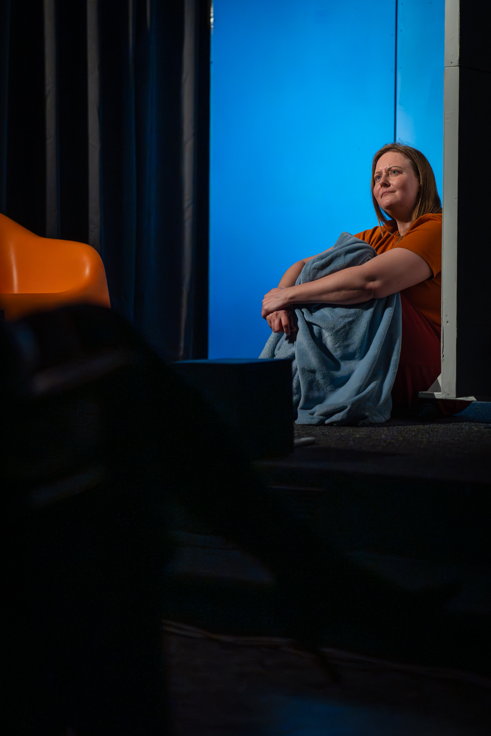 A woman sits huddled in a blanket, looking off into the distance