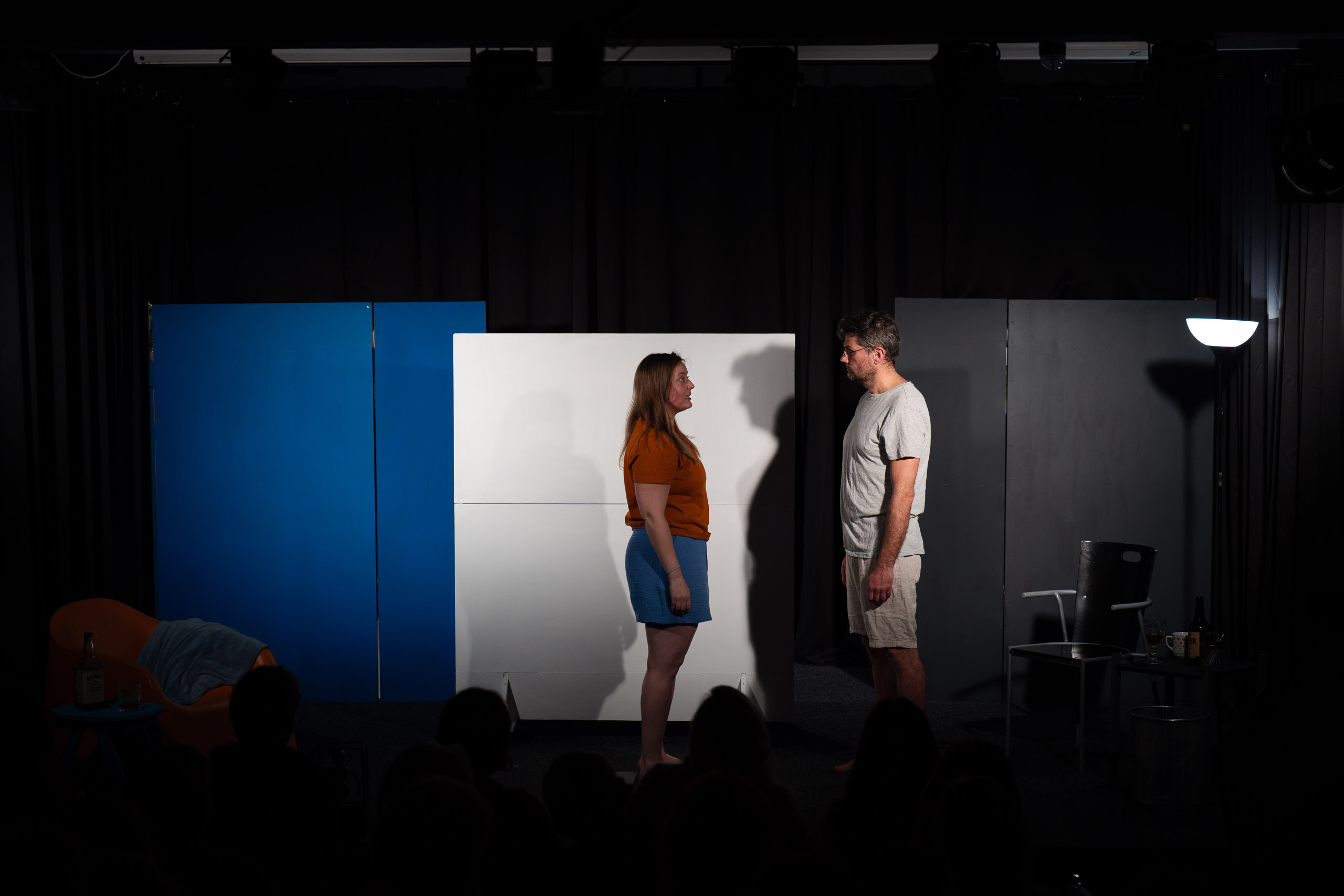 A man and a woman stand facing each other on a stage in front of