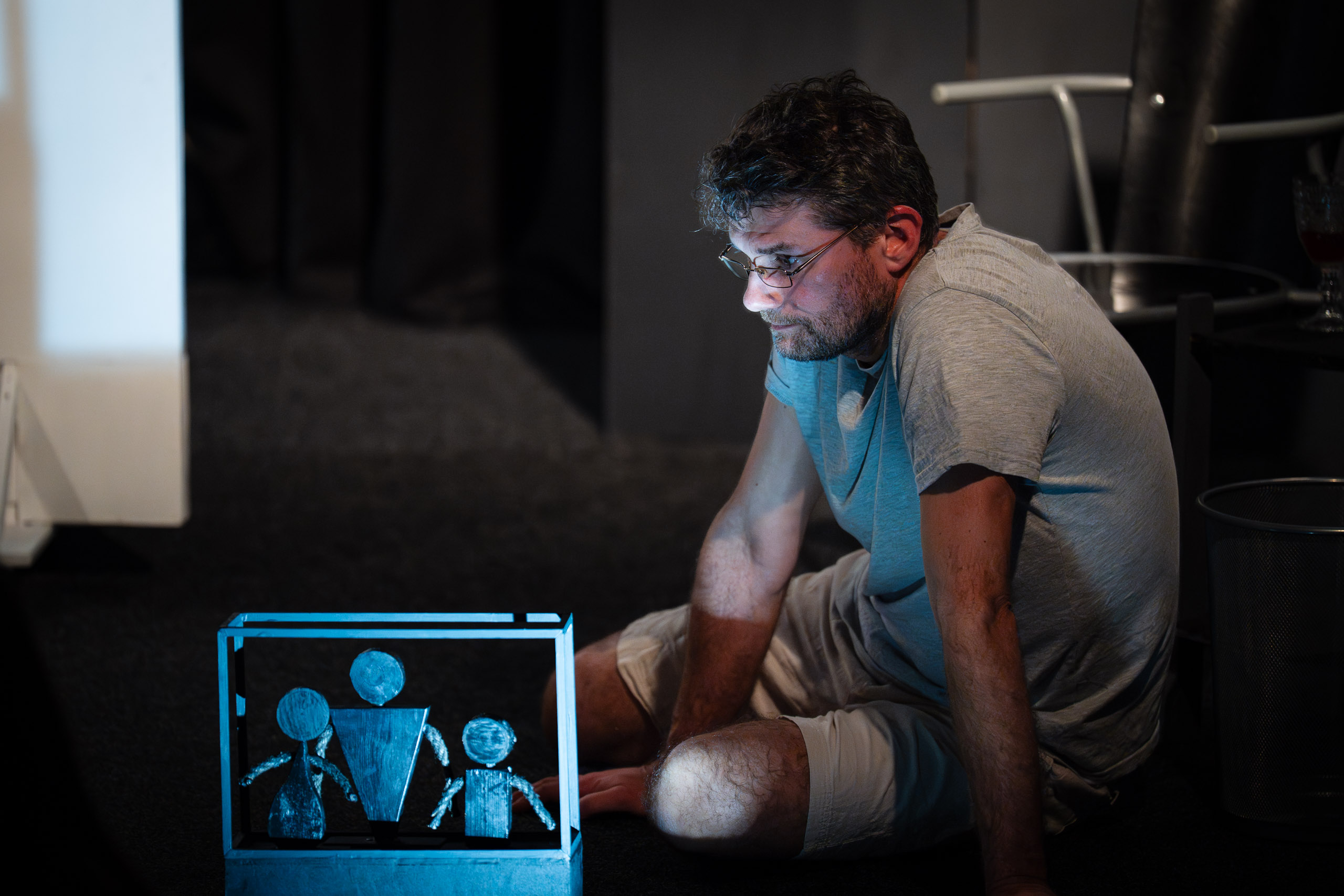 A man sits on the floor looking at a projection of a family.