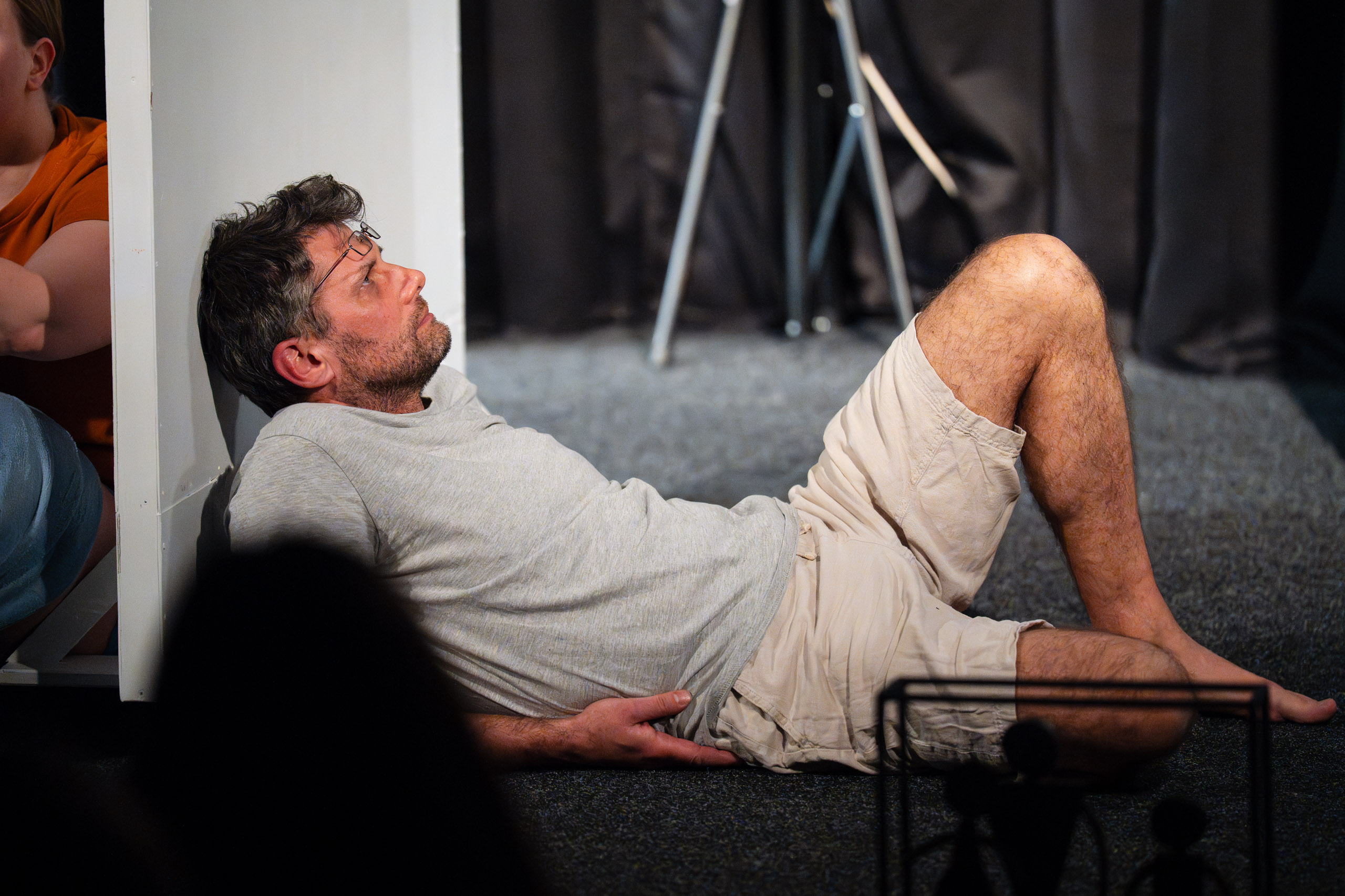 A man lies on the floor, leaning against a wall, looking up.