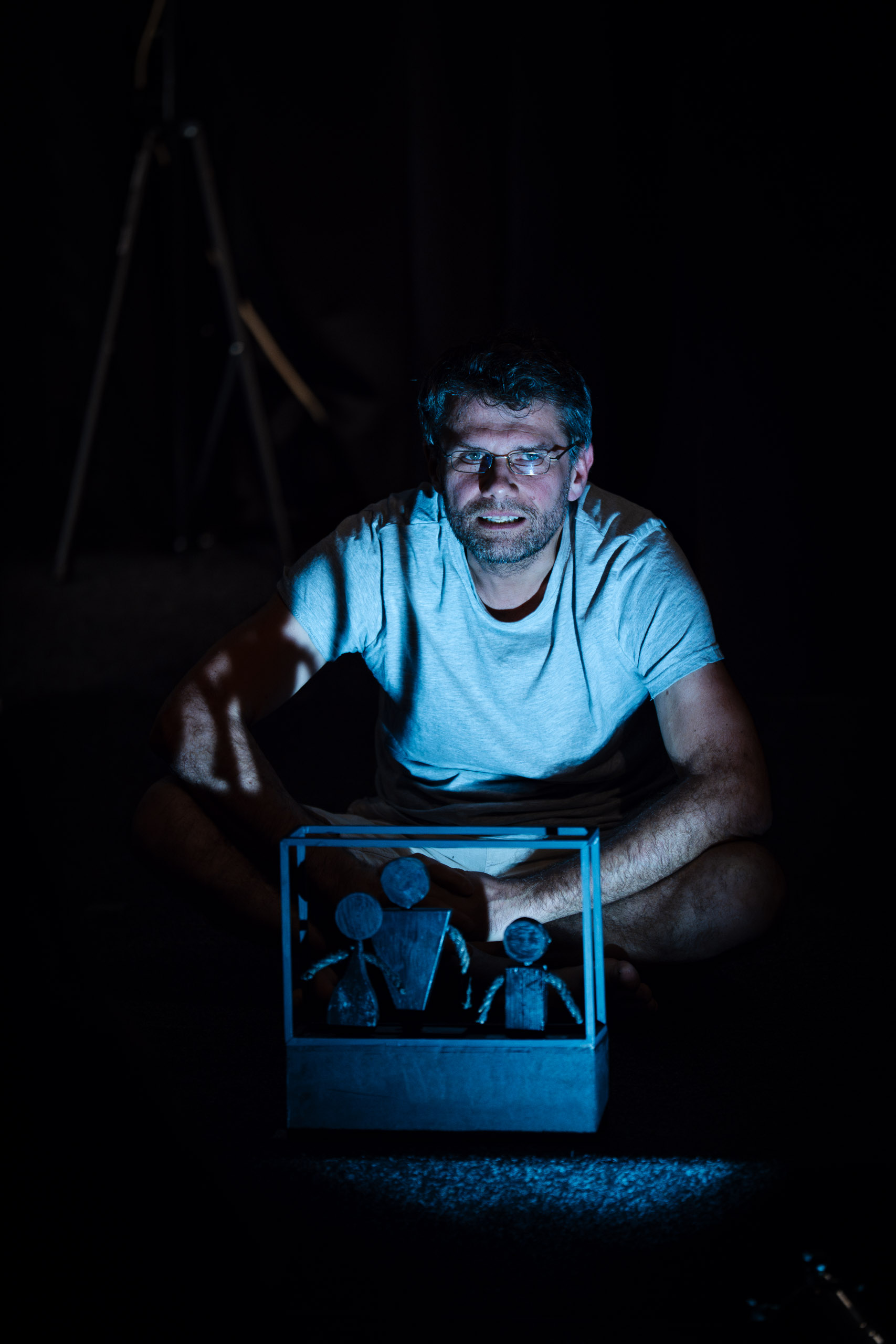 A man sits in the dark with a small diorama of a family in front