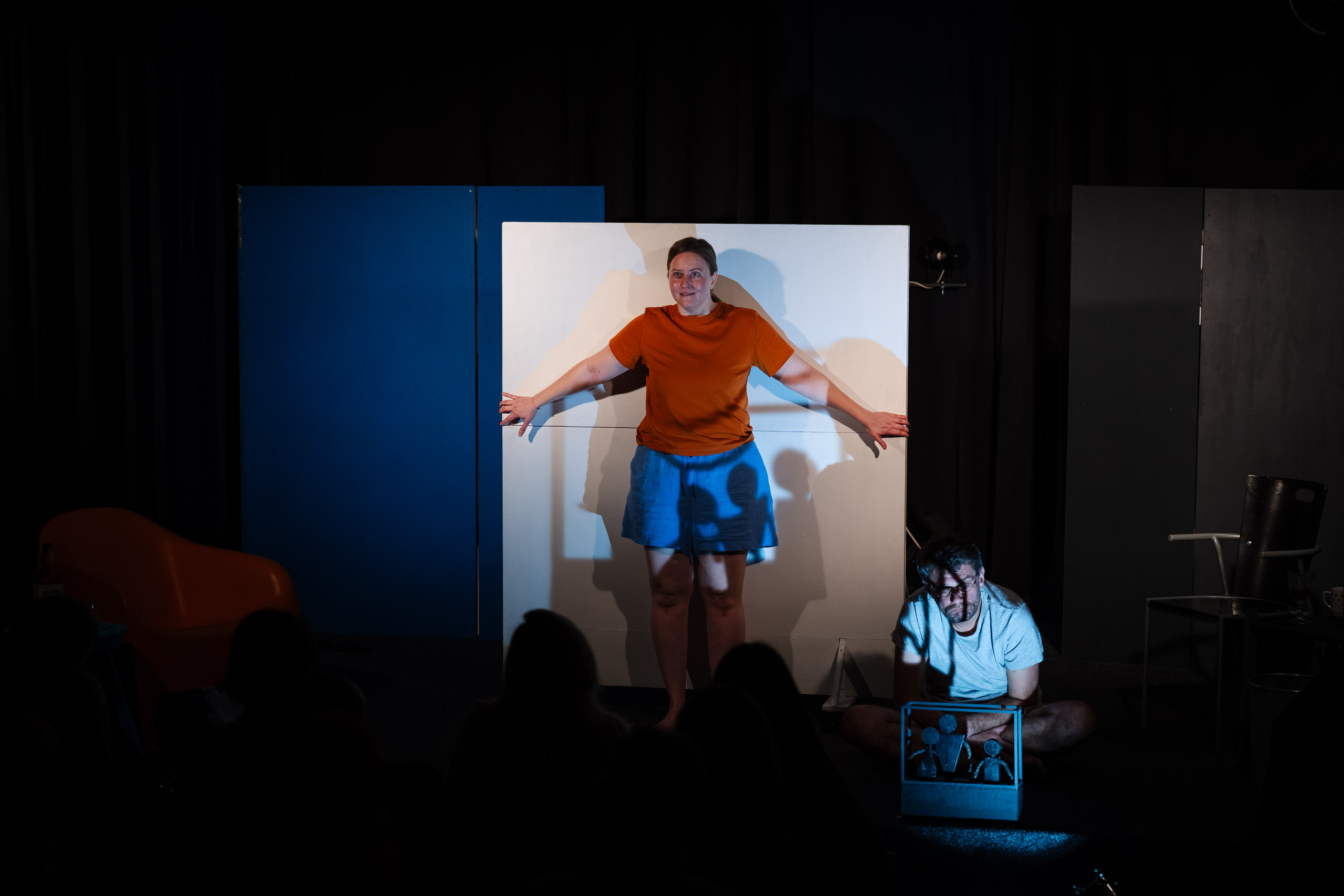 A woman stands with arms outstretched against a white panel, whi