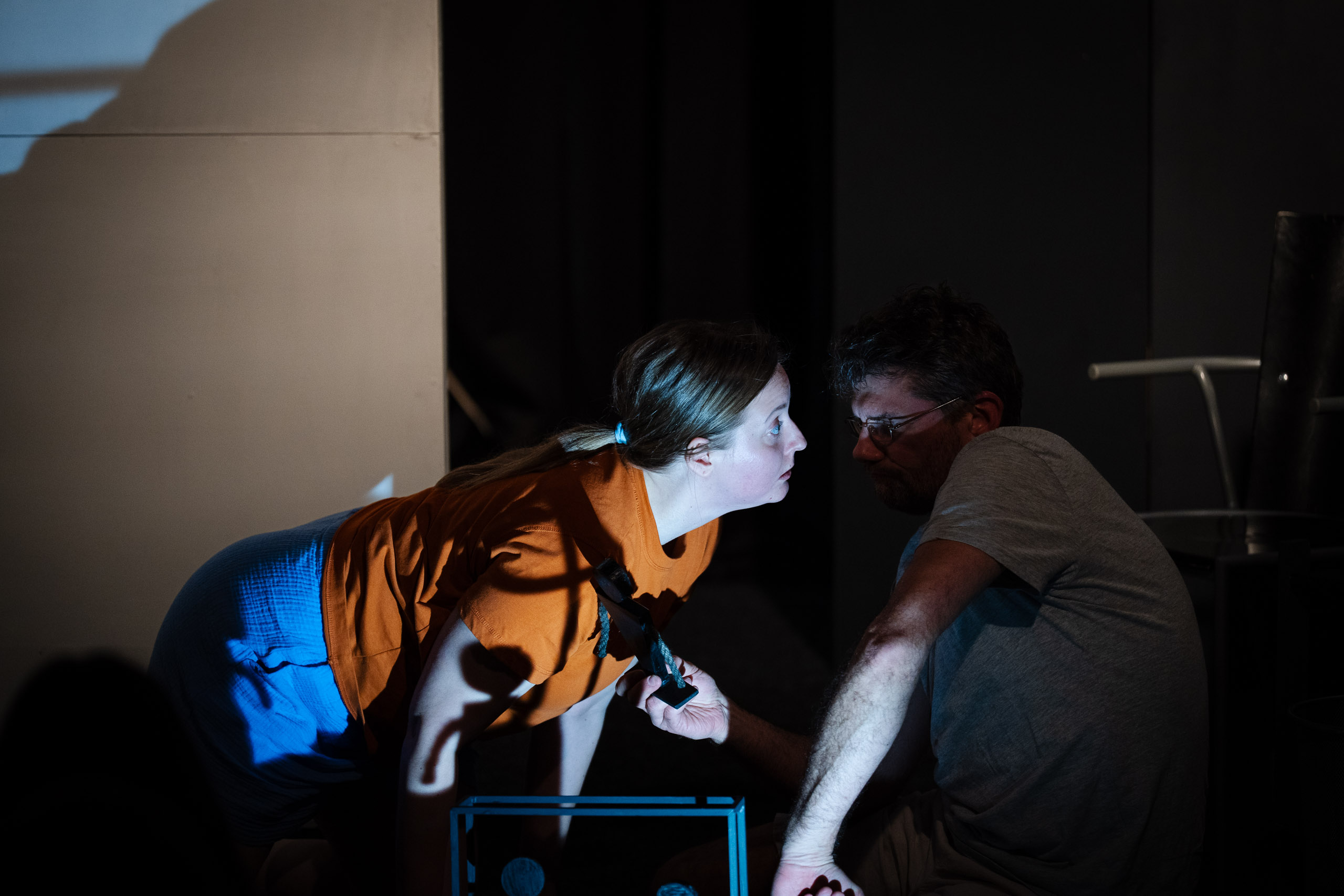 A woman in an orange shirt and blue shorts leans towards a man i