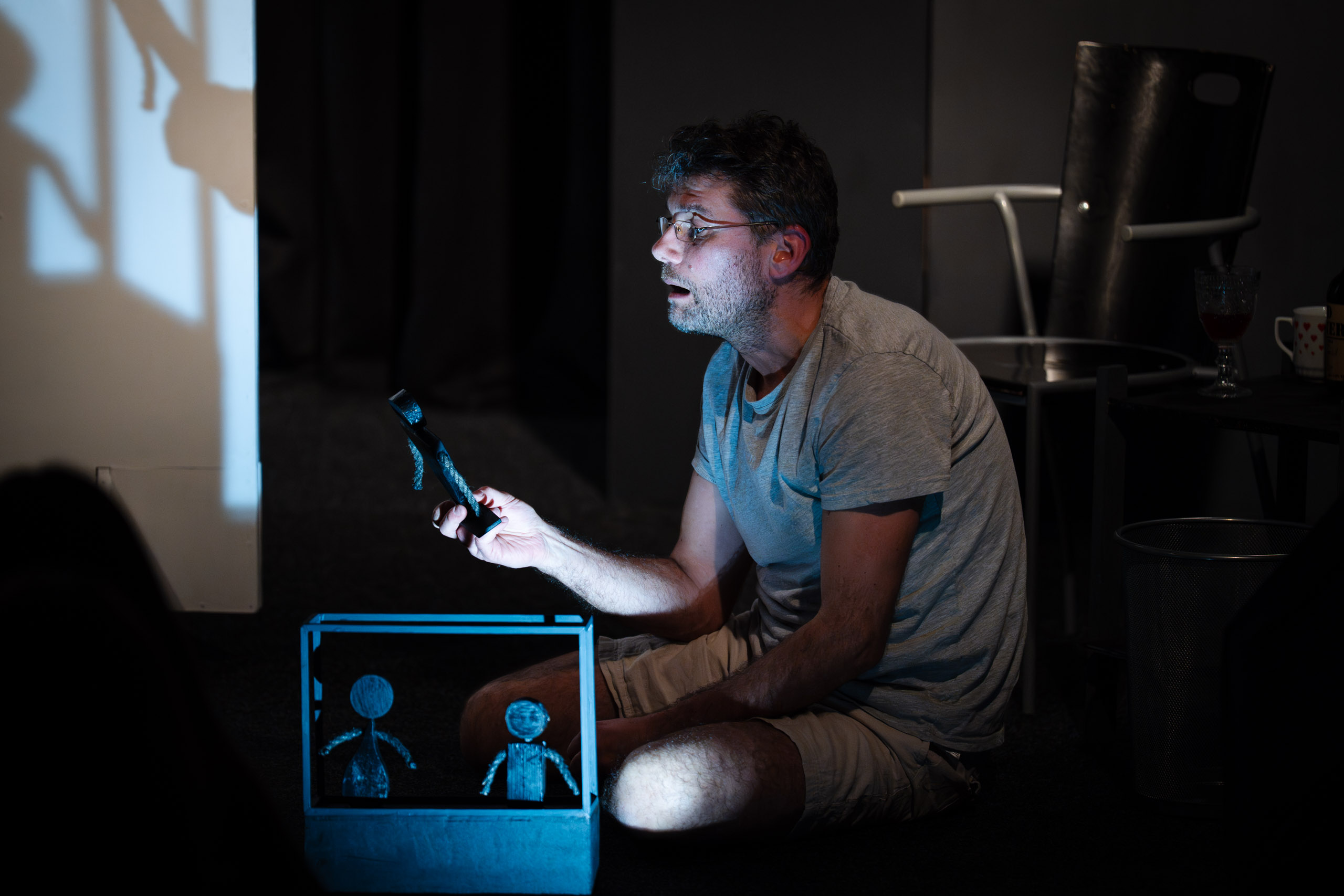 A man operates a shadow puppet show with a small stage and figur