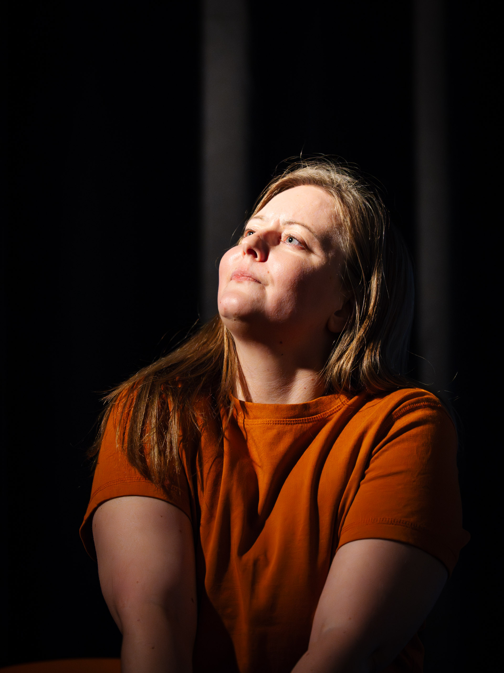 A woman looks up into a beam of light against a dark background.