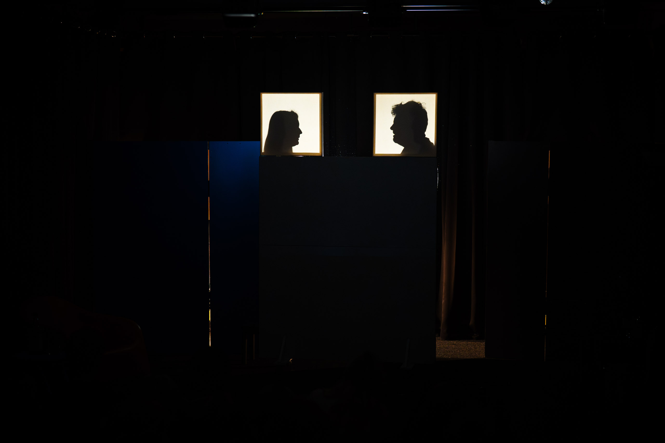 Silhouettes of a man and woman face each other in a dark room.