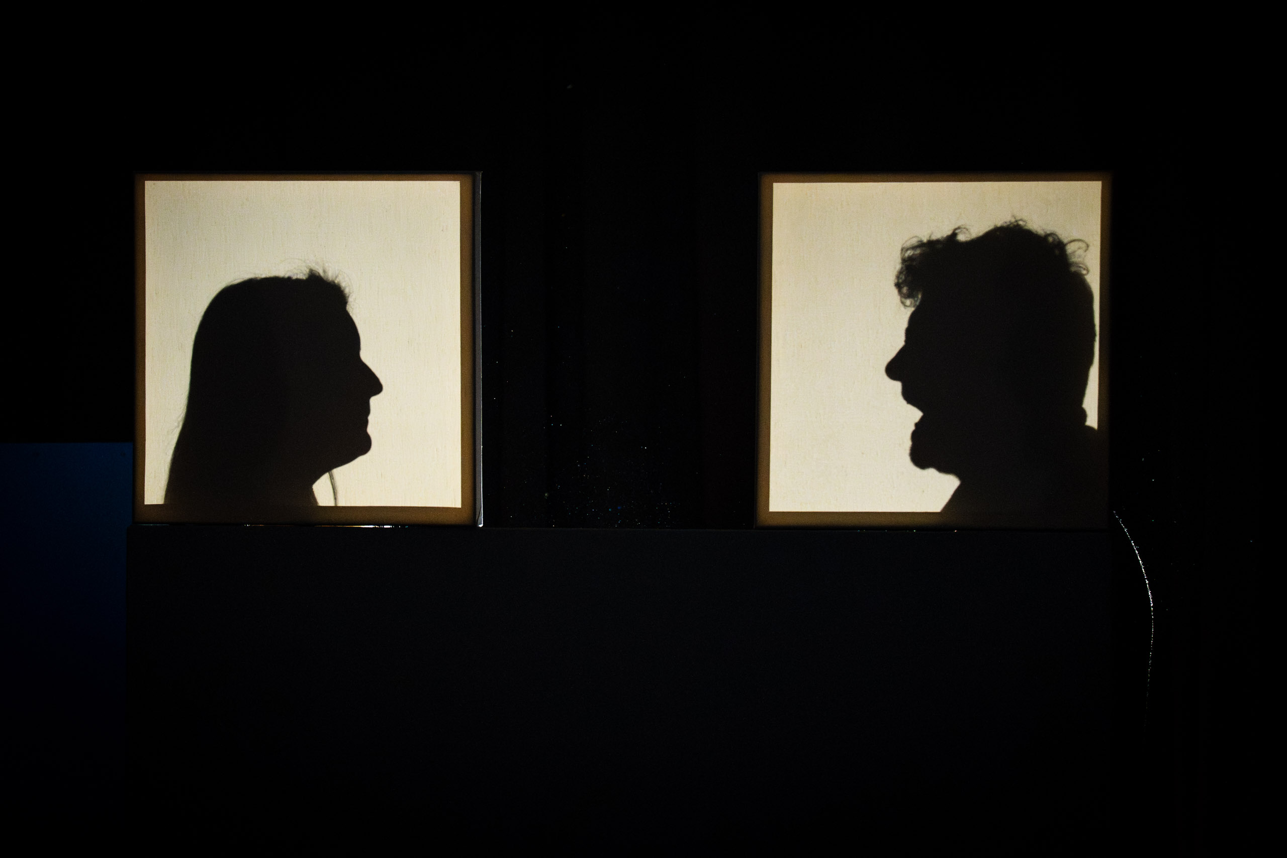 Silhouettes of a man and woman face each other in a dark room.
