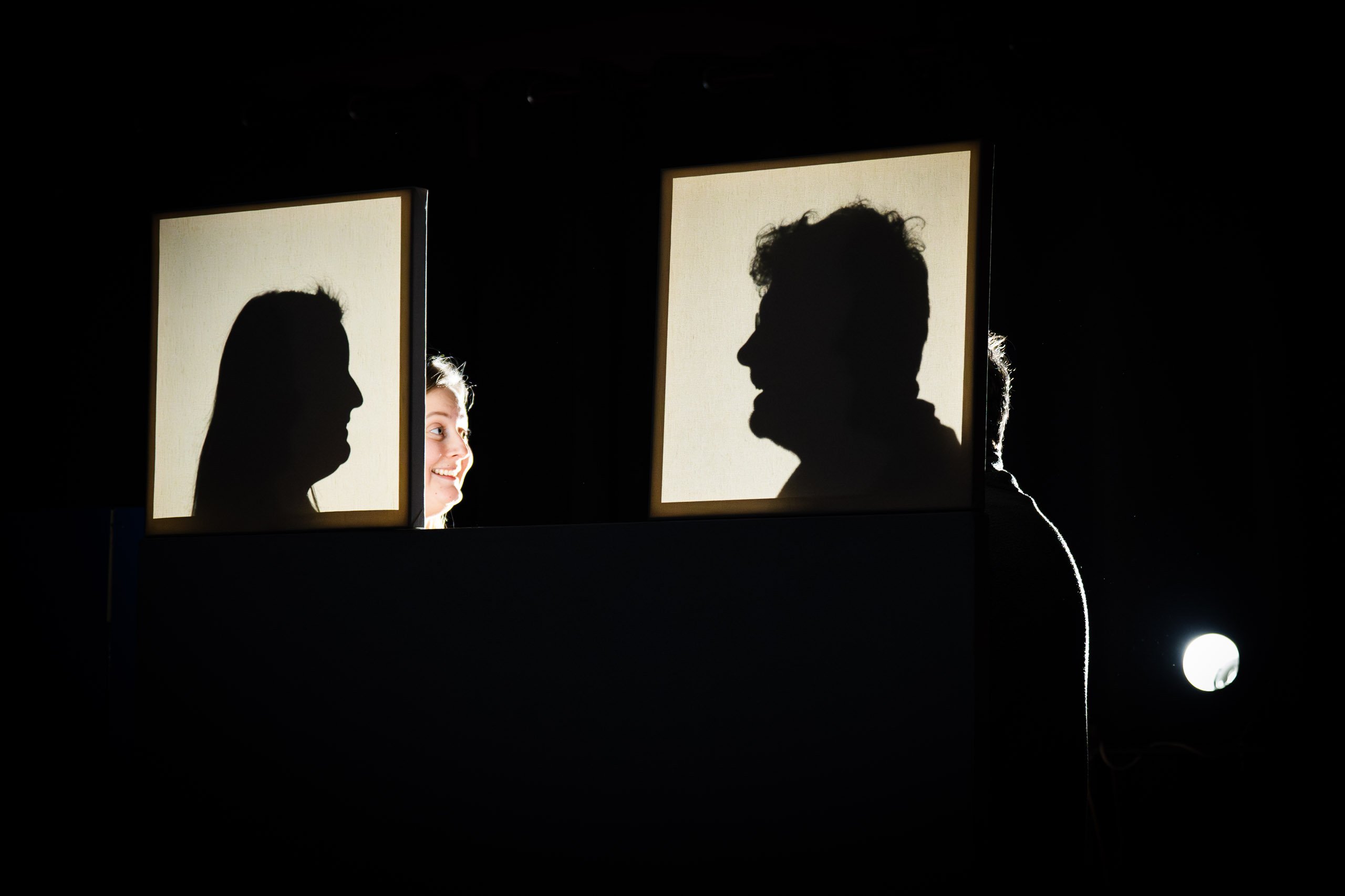 A woman smiles as she looks at a silhouette of a man, with anoth