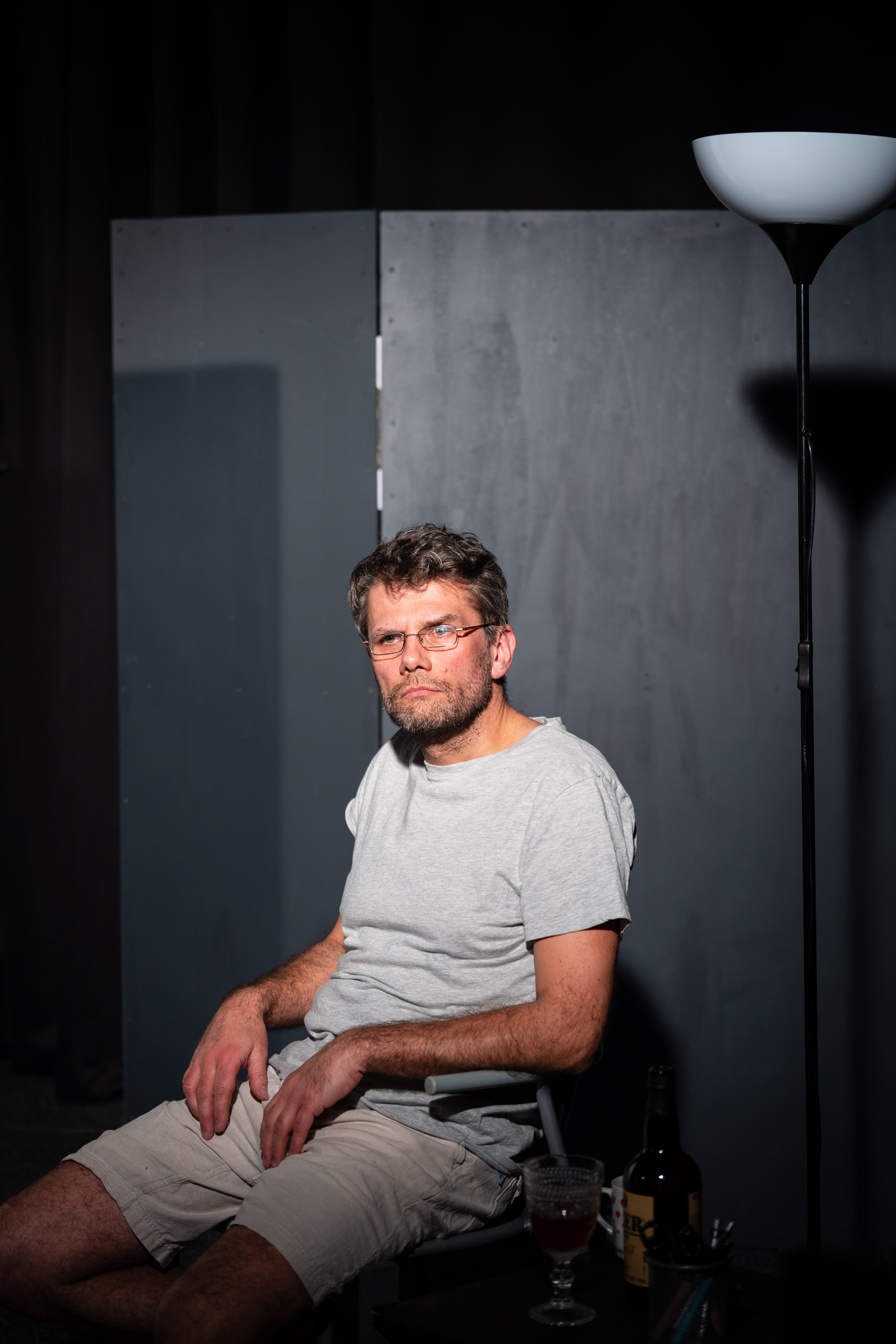 A man with glasses sits in a chair with a bottle of wine and a g