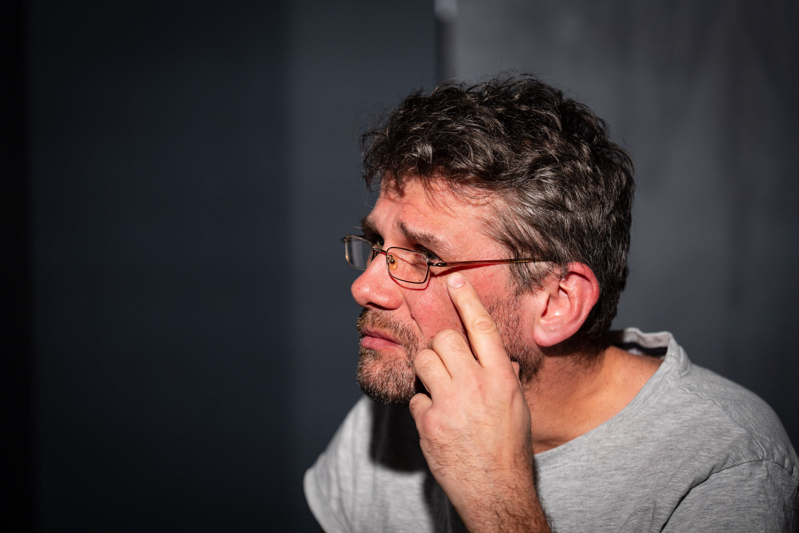 A man with glasses touches his face thoughtfully.
