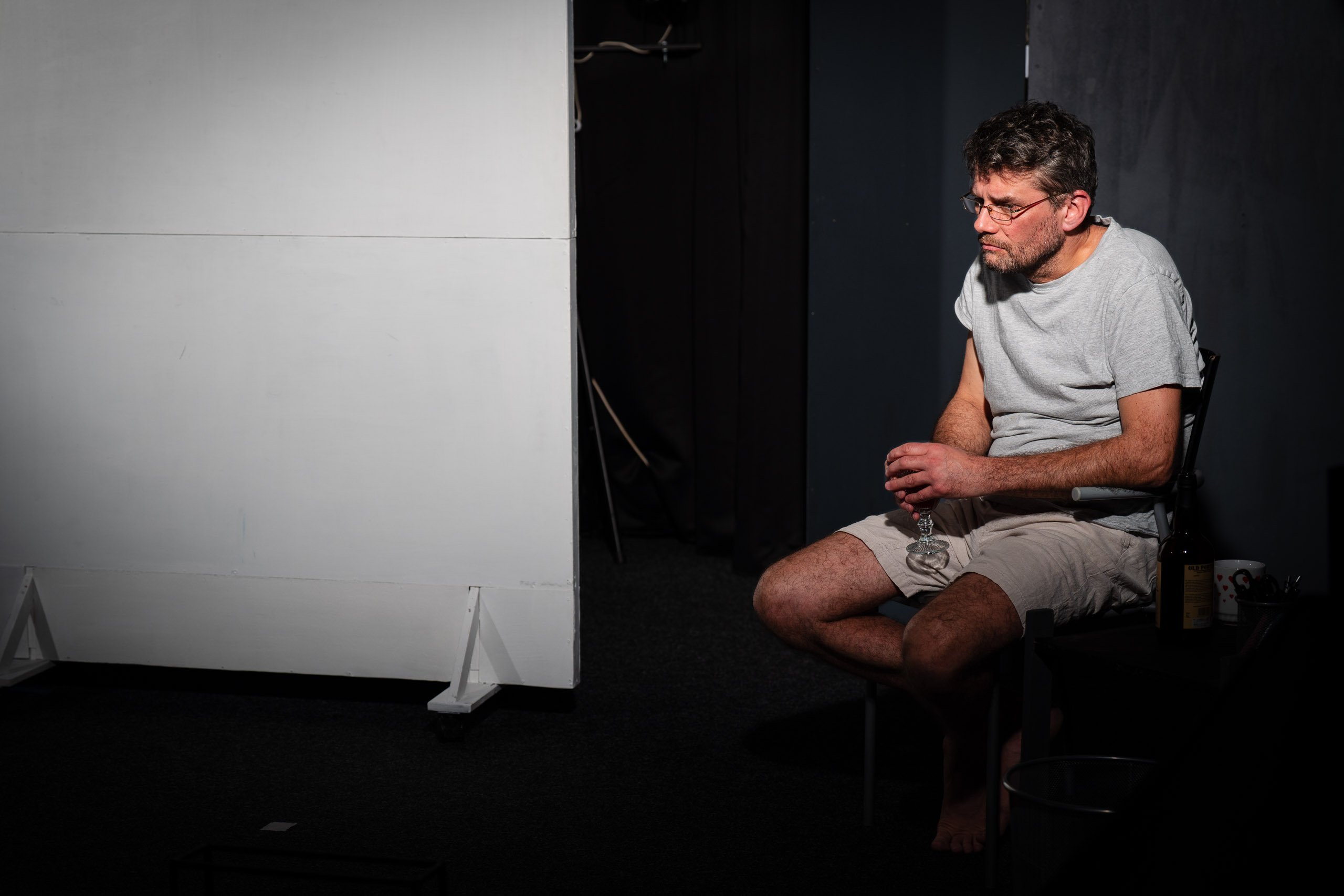 A man sits alone in a dimly lit room, holding a glass of wine.