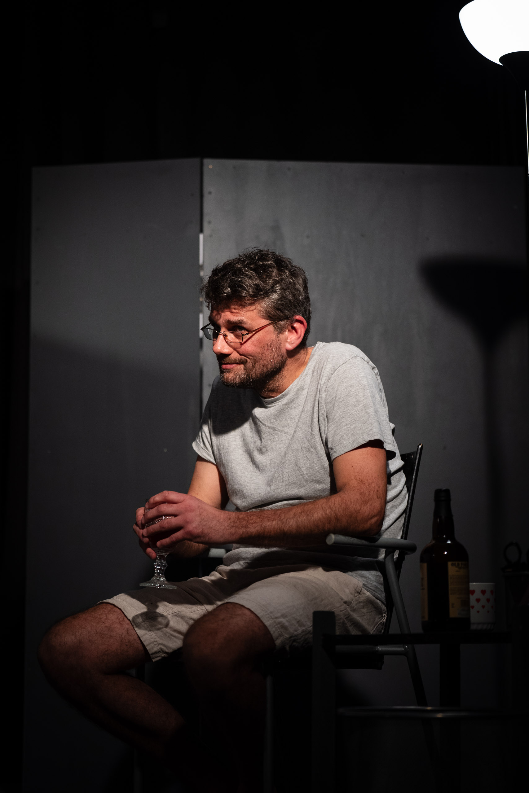 A man in glasses sits in a chair holding a glass of wine with a