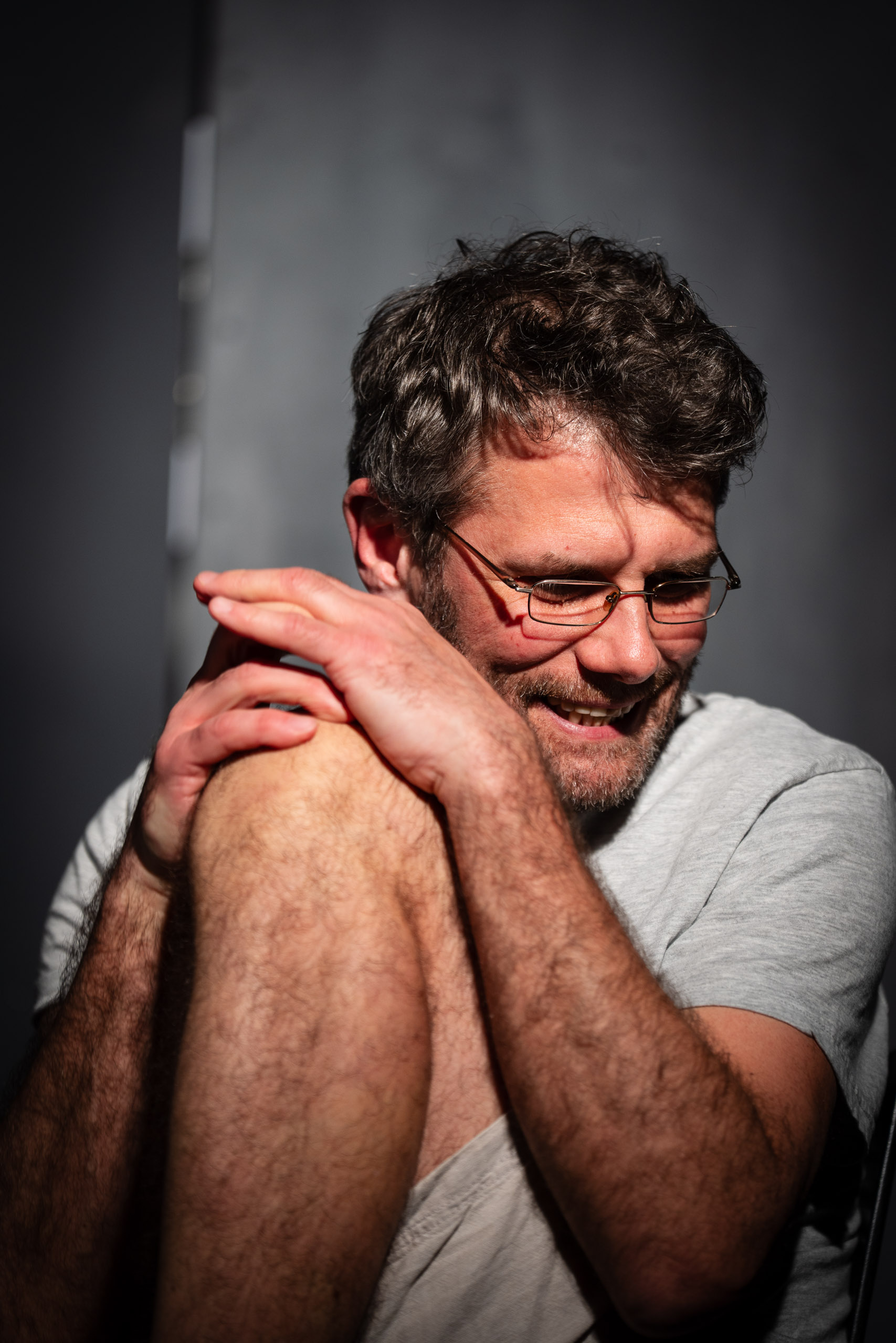 A man with glasses smiles and holds his knee.