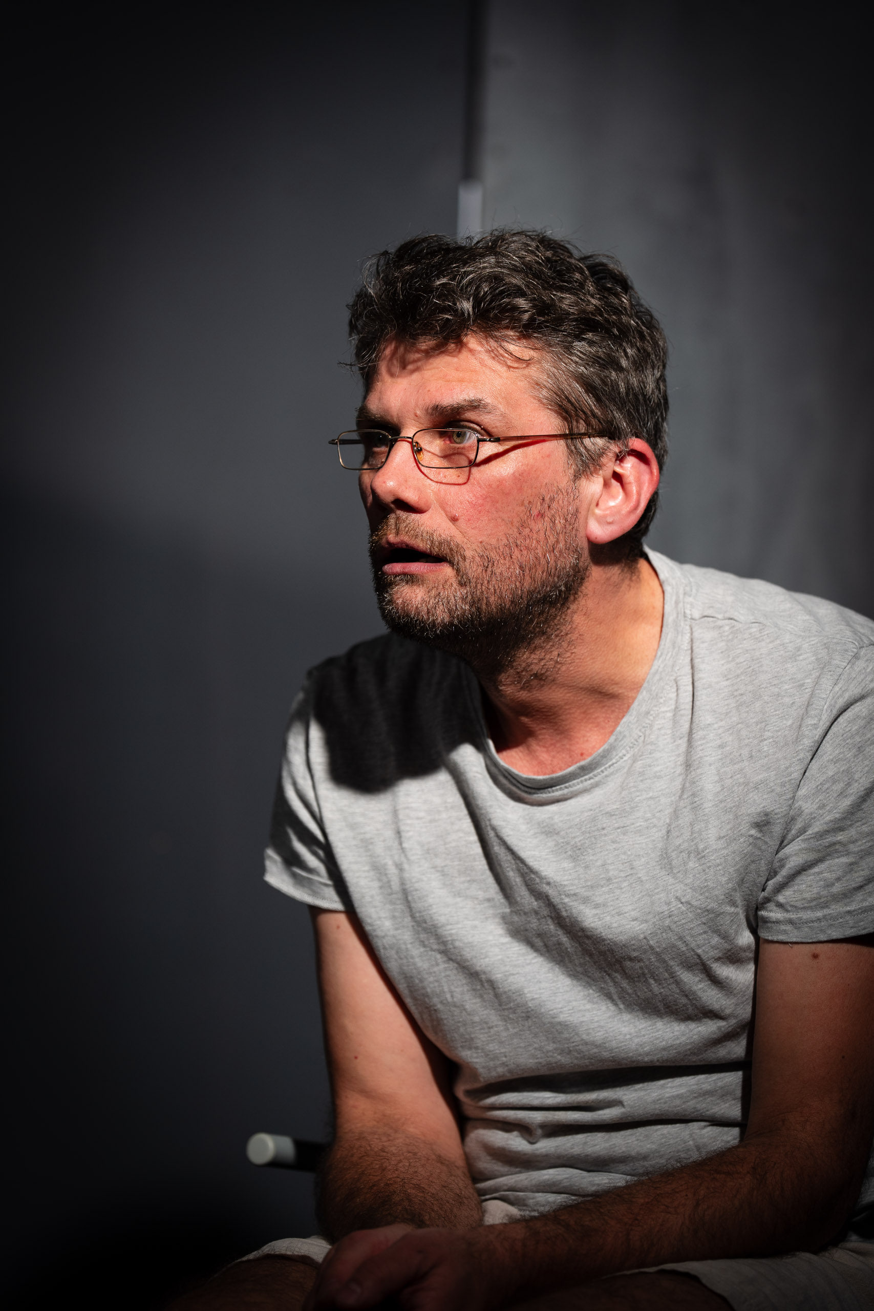 A man with glasses and a beard looks off to the side, illuminate