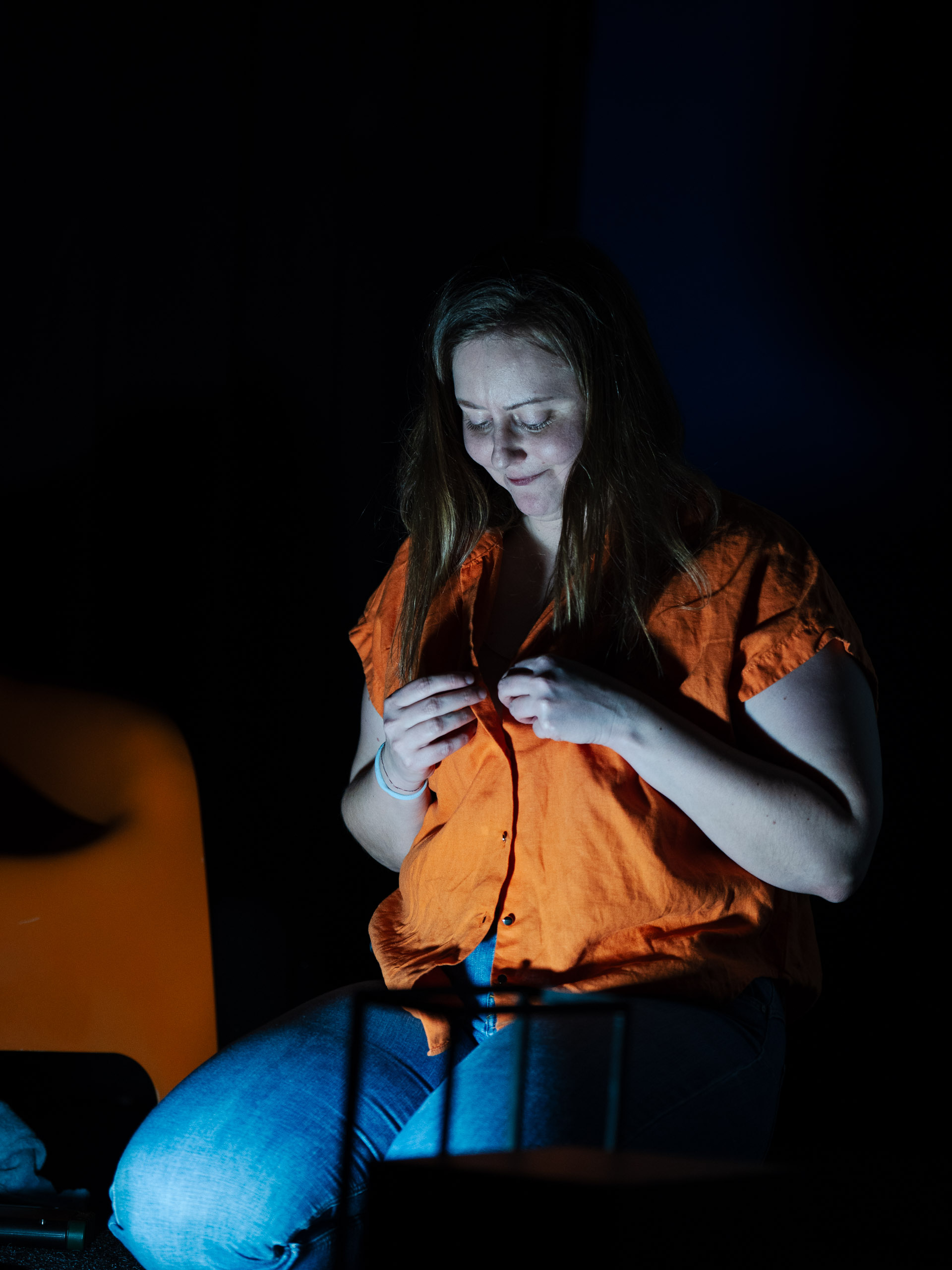A woman in an orange shirt and jeans buttons up her shirt in the